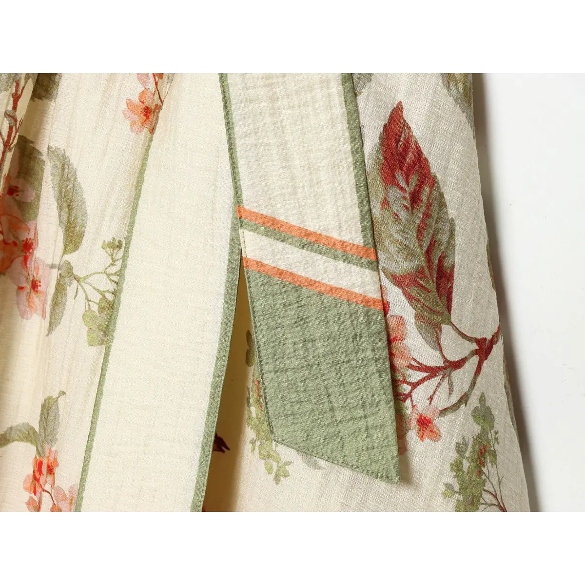 Close of printed waist sash tail, green piped edge + dual orange-white stripe accent matching dress hem border.
