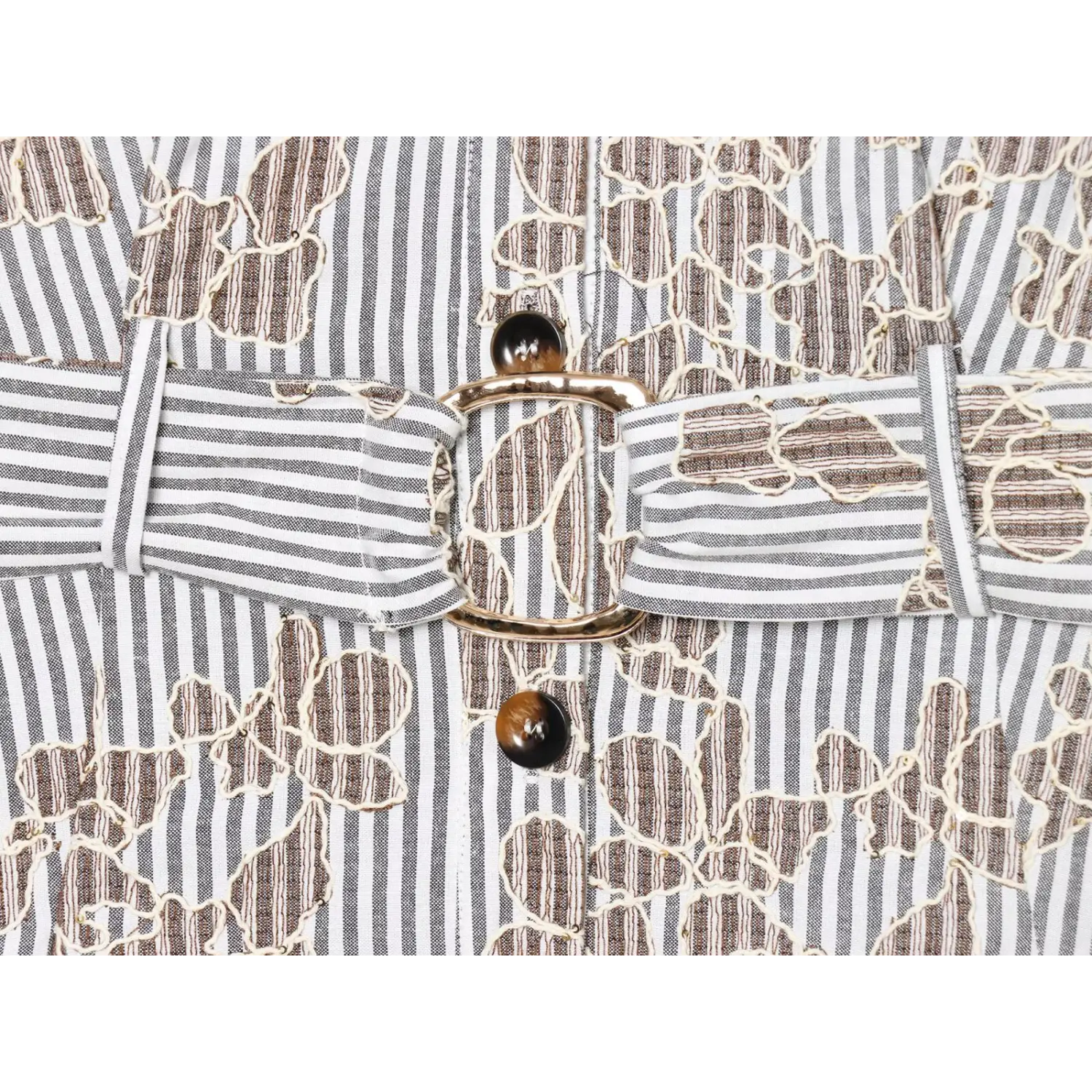 Macro shot of gold‑tone belt buckle, tortoiseshell button and striped floral fabric