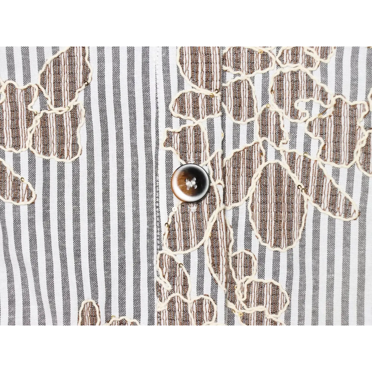 Macro shot of tortoiseshell front button over mixed stripe floral embroidered woven fabric