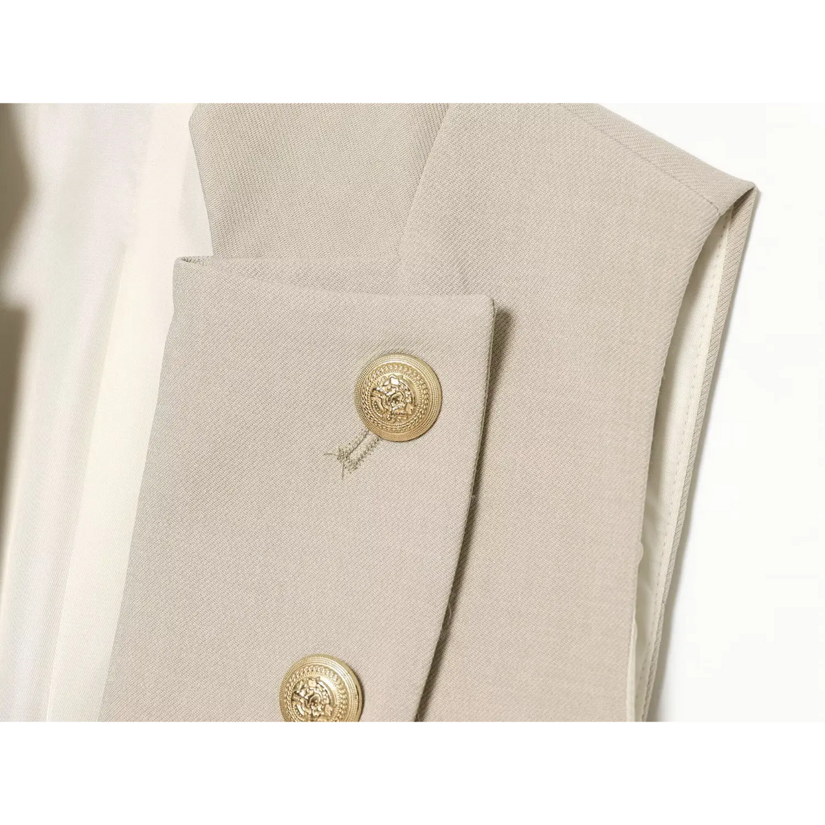 Close‑up embossed gold metal button texture on beige waistcoat