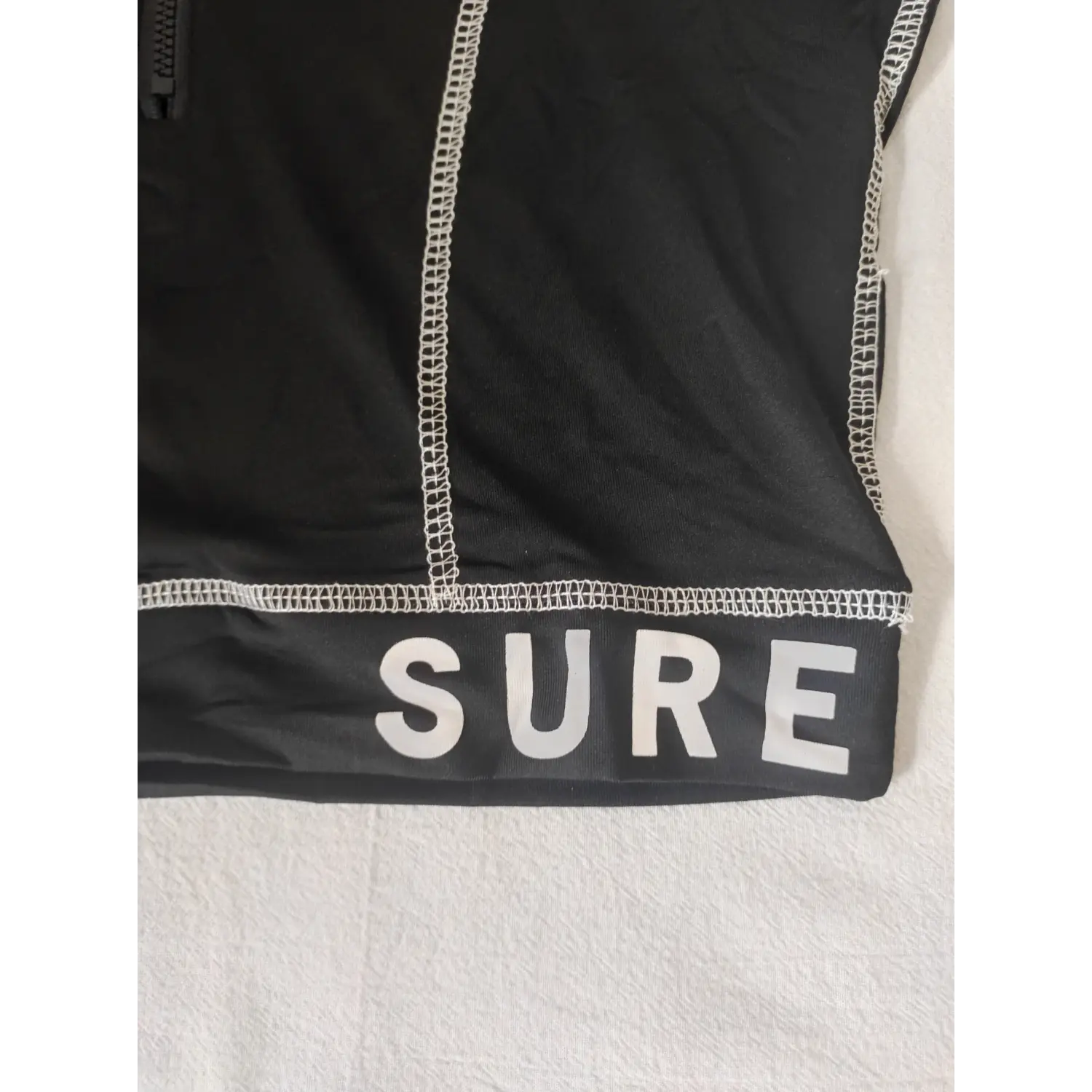Extreme close-up white SURE letter print and hem stitching on black cropped long sleeve top
