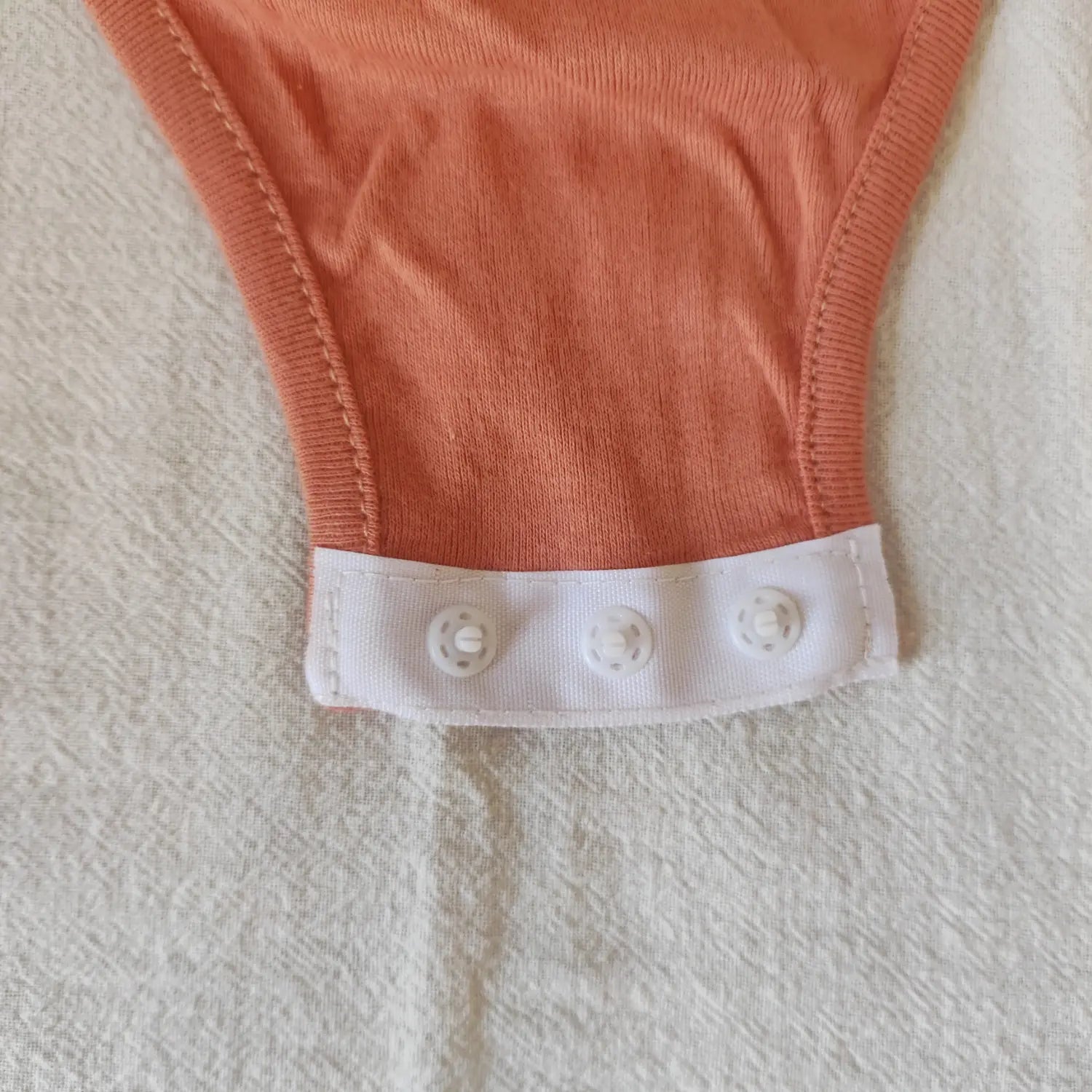 Extreme close‑up white plastic snap buttons at crotch on terracotta long sleeve bodysuit