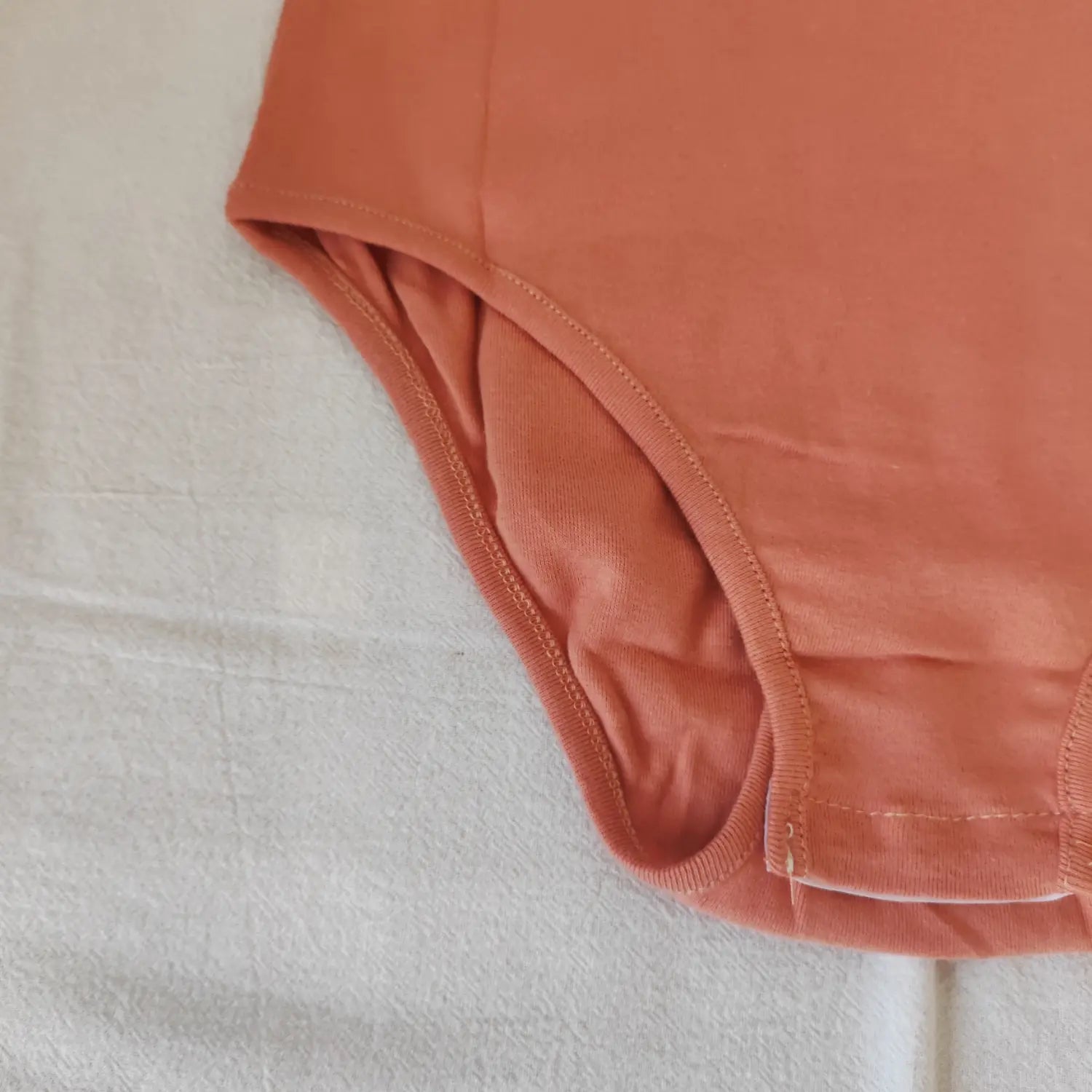 Close‑up leg opening finished seam and stretch knit fabric of terracotta bodysuit