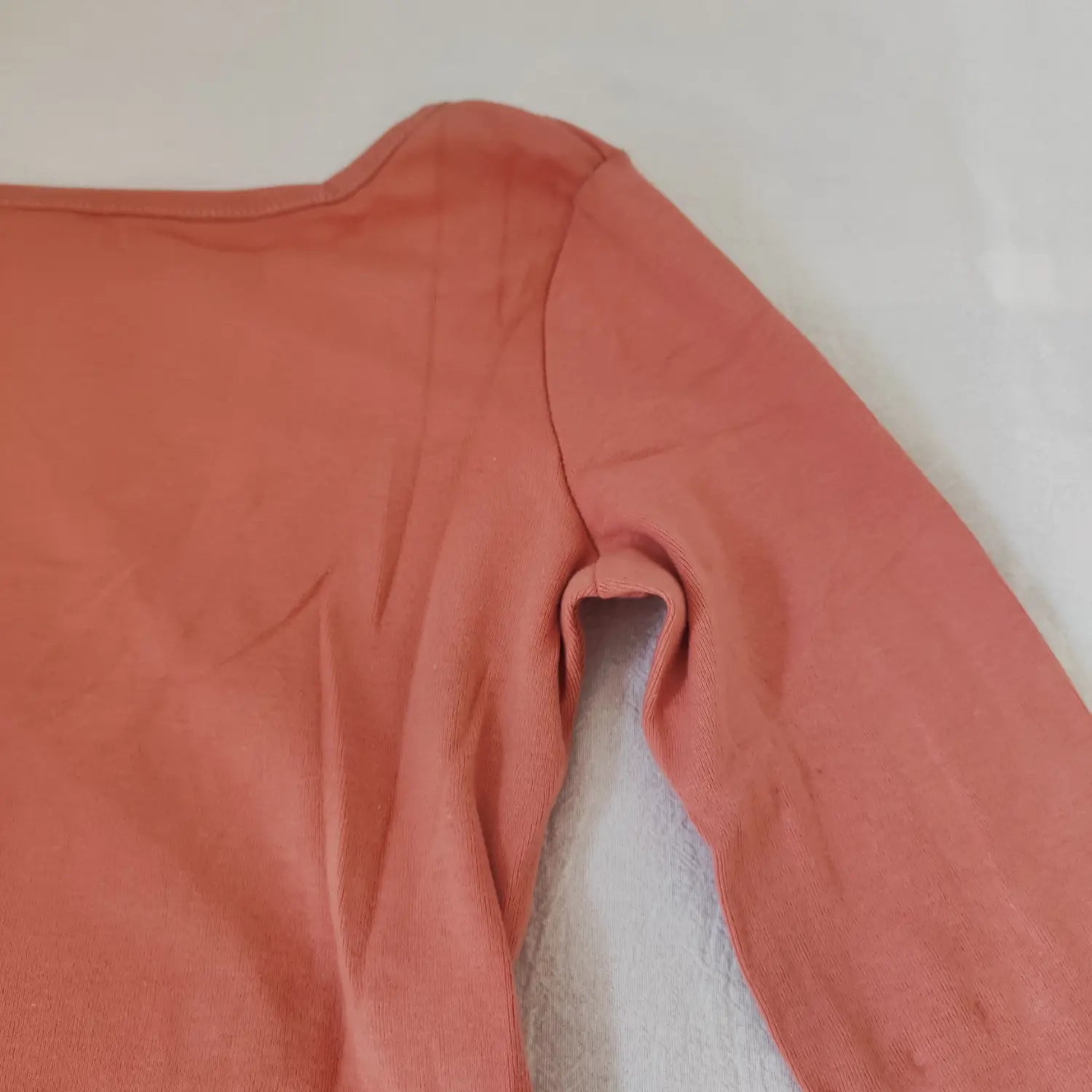 Close‑up shoulder and armhole stitching construction on terracotta long sleeve bodysuit