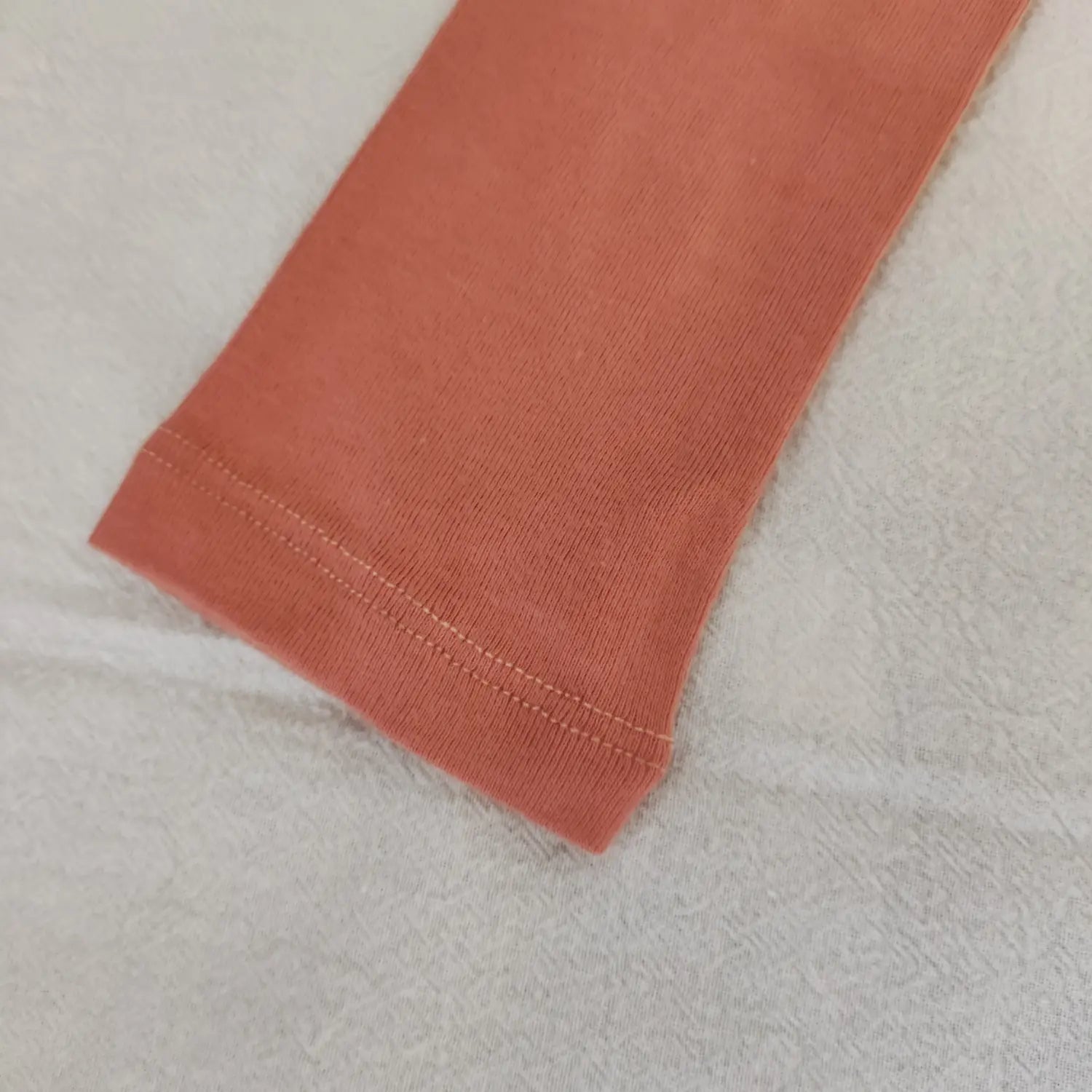 Close‑up double stitched sleeve cuff hem detail of terracotta knit bodysuit