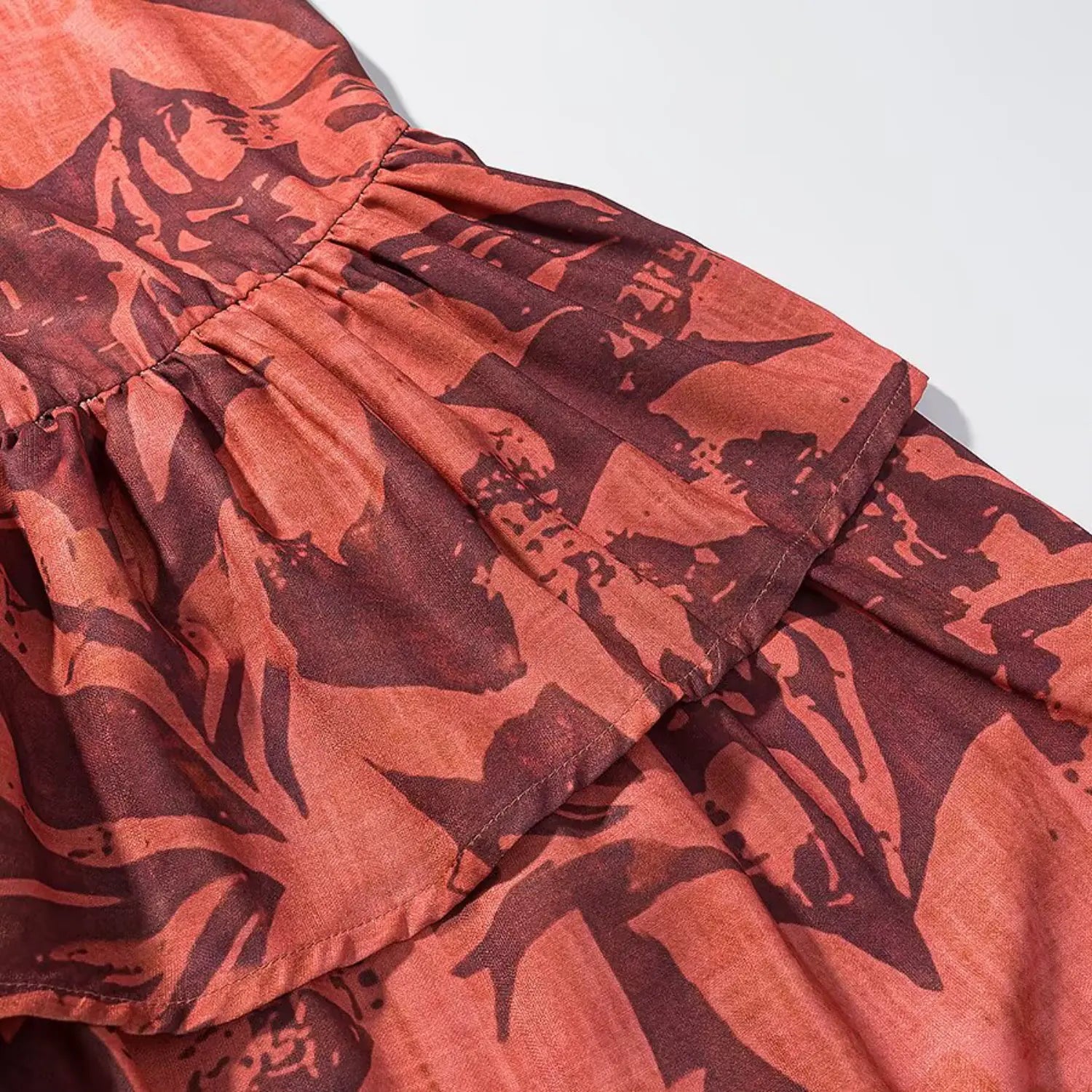 Close‑up of gathered seam at tiered ruffle hem of terracotta floral halter midi dress