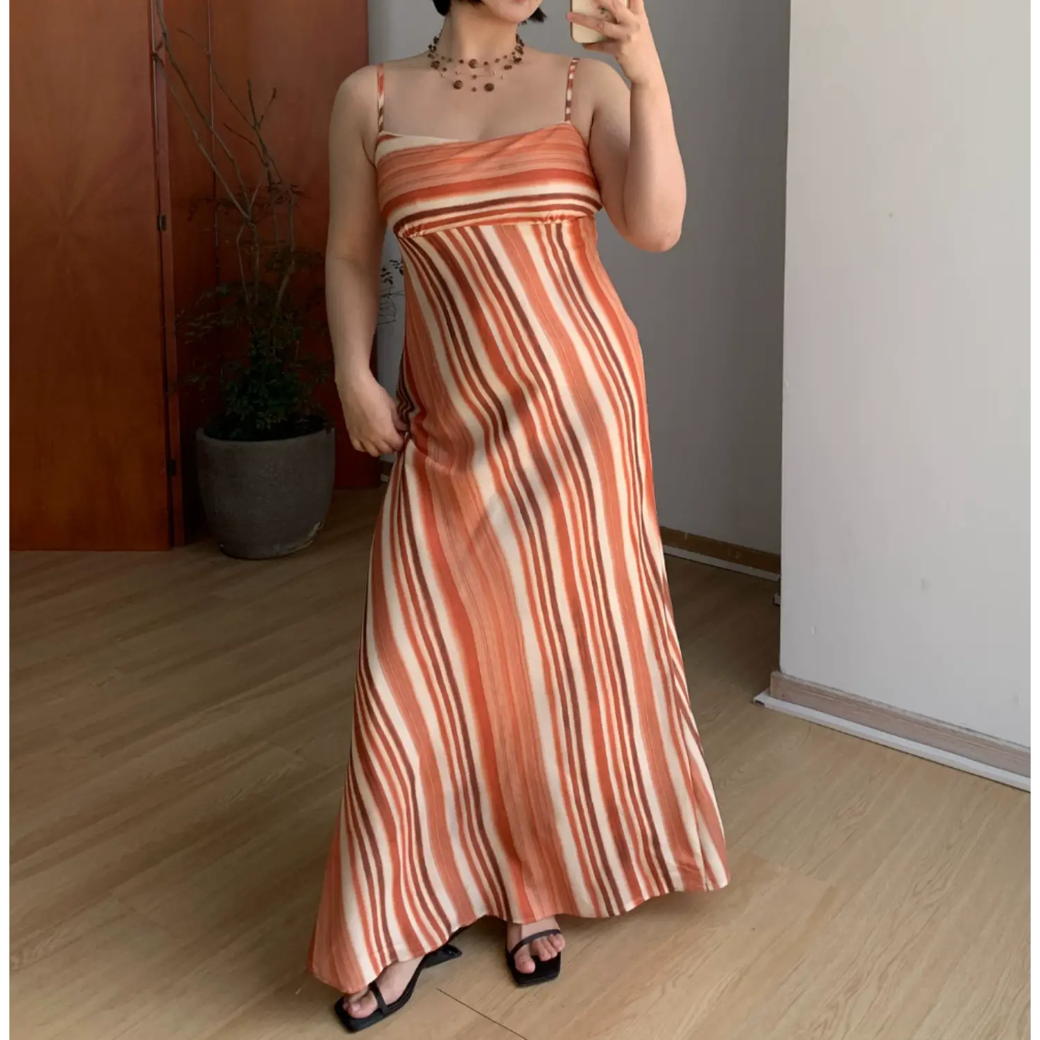 Indoor mirror full shot of cream base terracotta vertical gradient stripe slip maxi dress, thin adjustable spaghetti straps, fitted empire waist, paired with simple black square slide sandals
