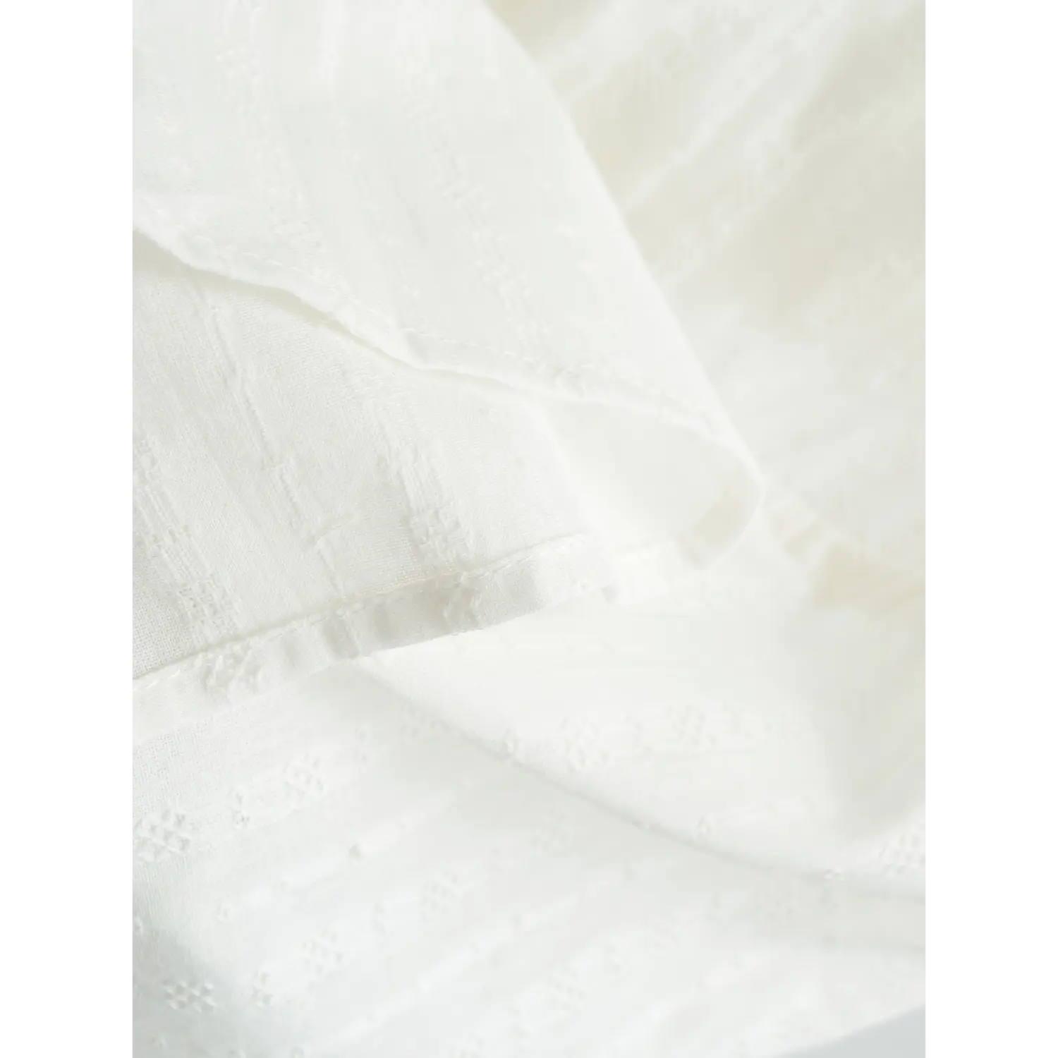 Close-up of the textured fabric with geometric patterns on a white camisole