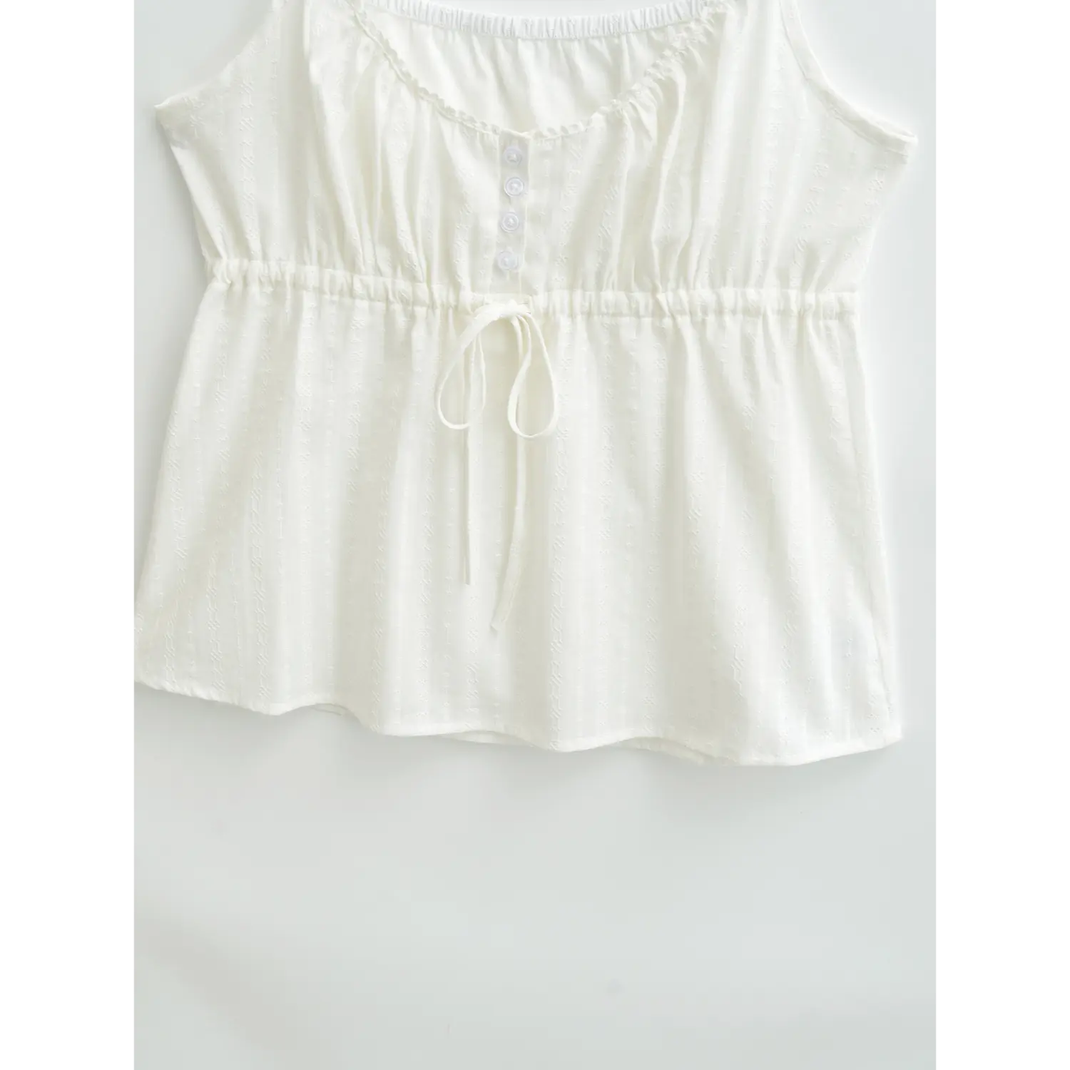  Full front view of a white textured camisole laid flat, showing the button placket and drawstring detail