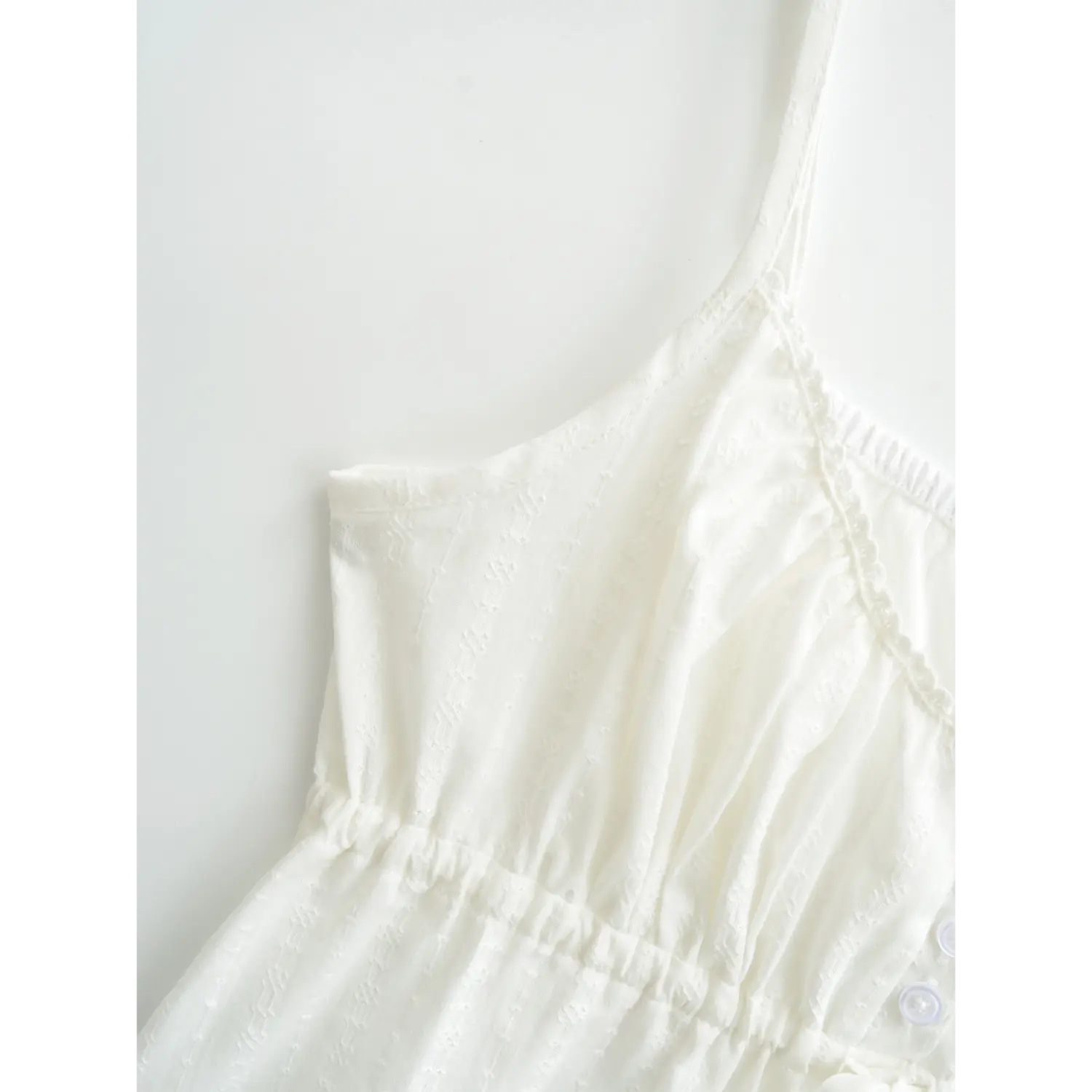 Close-up of the adjustable spaghetti strap and lace-trimmed neckline on a white textured camisole