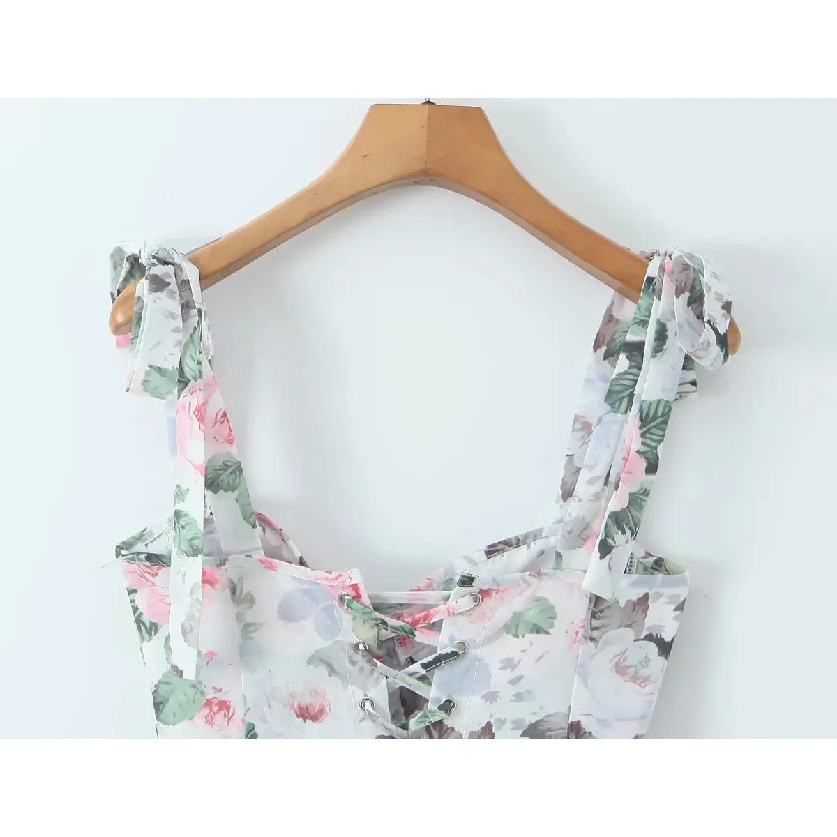 Close-up of the floral print tie straps and corset bodice on a dress hanging on a wooden hanger.
