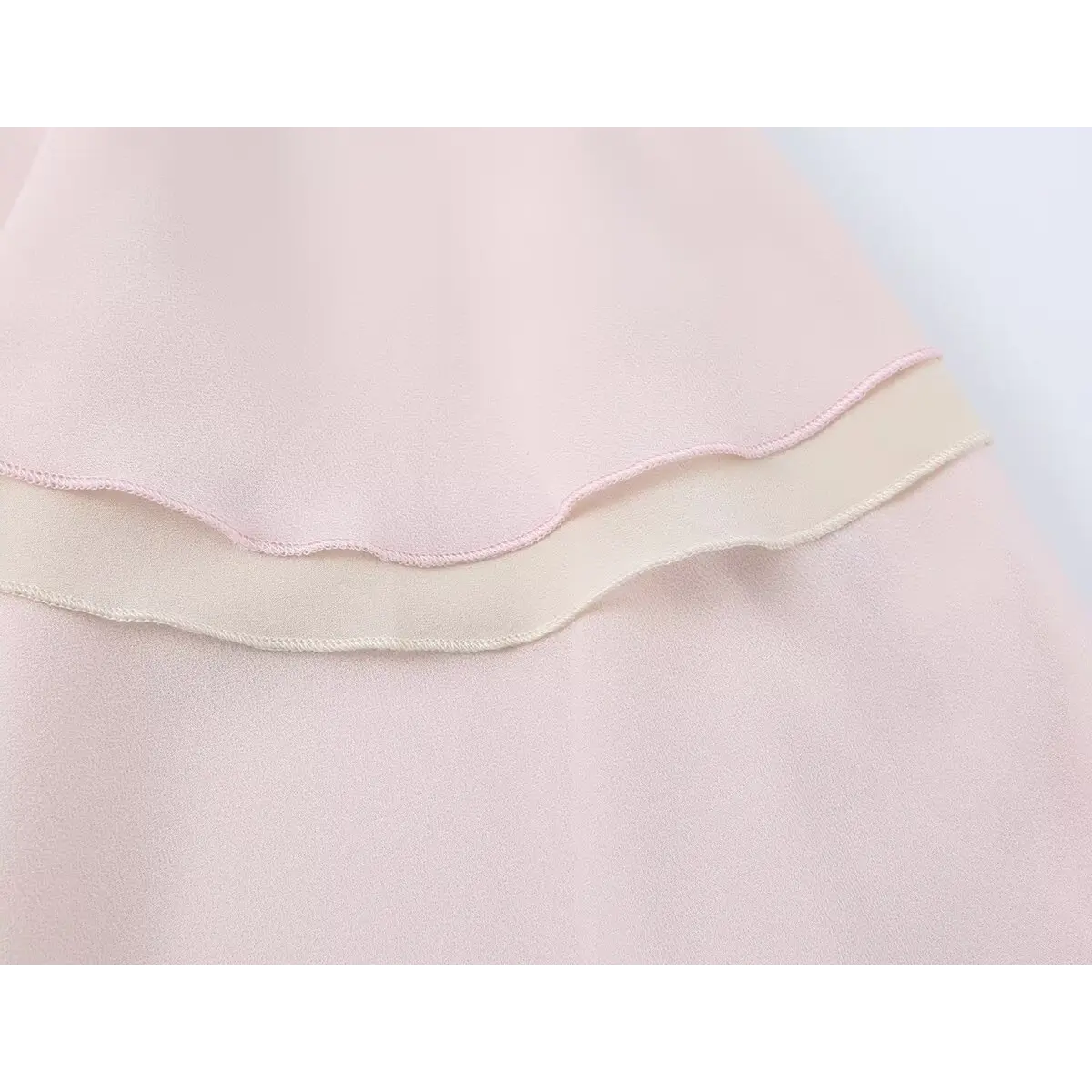Close-up of the hem on a pink tiered chiffon skirt, highlighting the contrast between the pink and beige layers.
