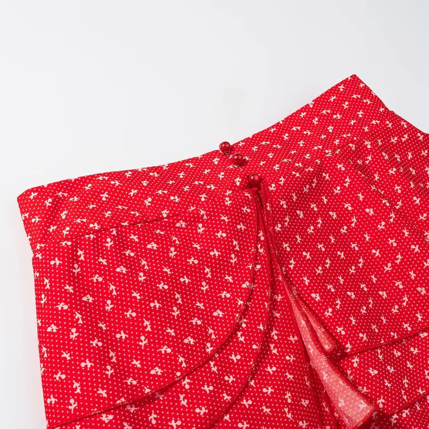 Close‑up of waist wrap and pearl buttons on red tiered ruffle mini skirt