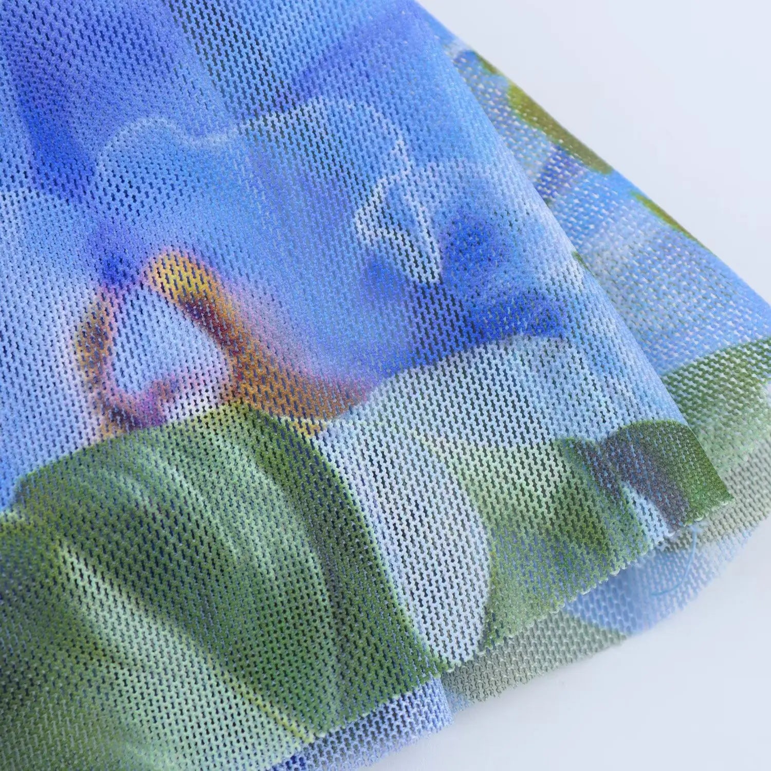 Macro fabric shot of sheer mesh material with vibrant blue tropical floral and green leaf print