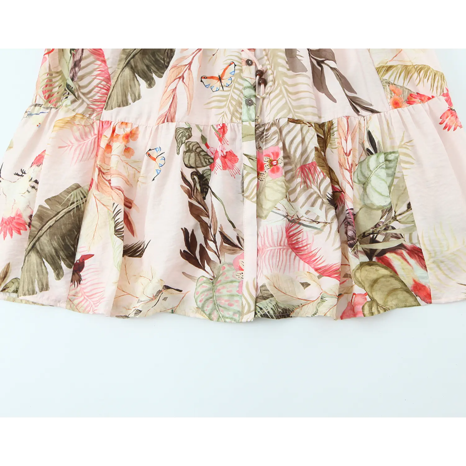 Close up of tiered ruffle skirt with tropical plant and butterfly print on pink midi dress