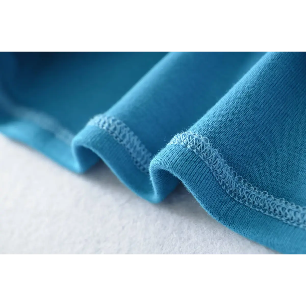 Close-up of the fabric texture and overlock stitching on the turquoise camisole's hem