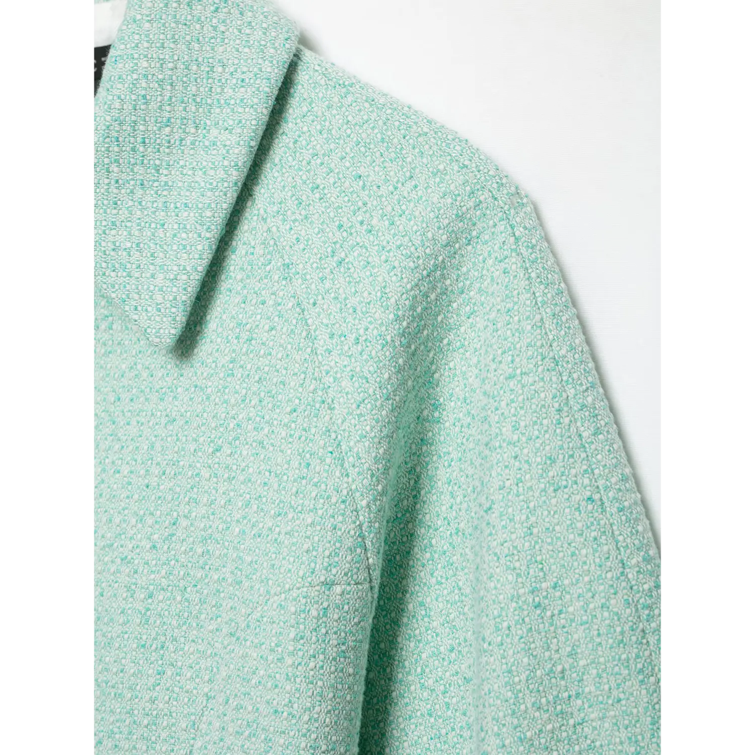 Extreme close-up mint green bouclé tweed fabric, shoulder raglan seam texture detail