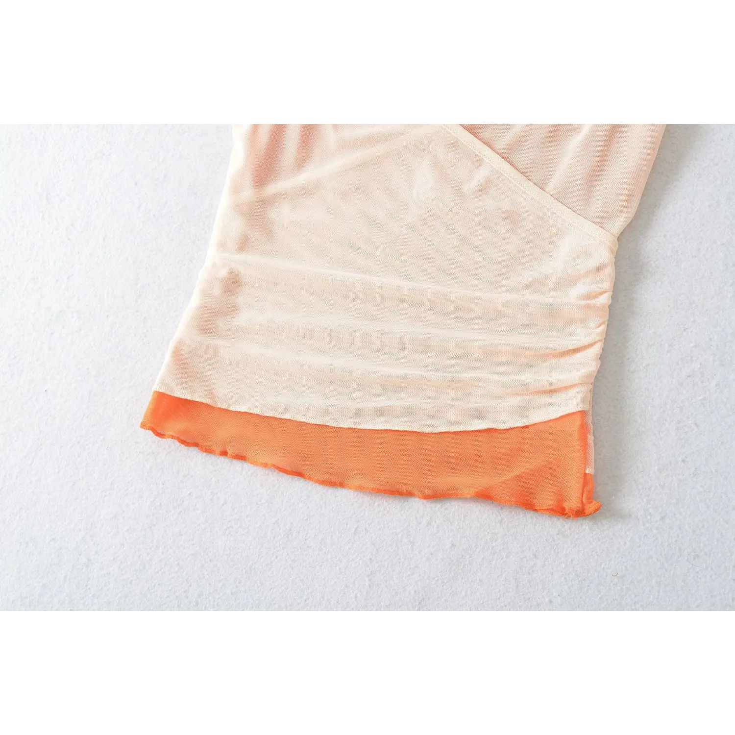 Two layer mesh cami hem wavy ruffle macro flat close-up, outer pale apricot mesh inner orange mesh spliced wavy overlock hem breathable mesh fabric white craft shot
