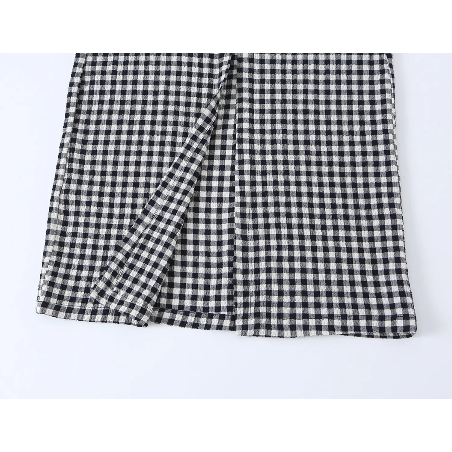 Gingham style skirt slit close-up, black white check crinkle woven fabric, vertical split seam, neat hem stitching, bubble texture plaid material
