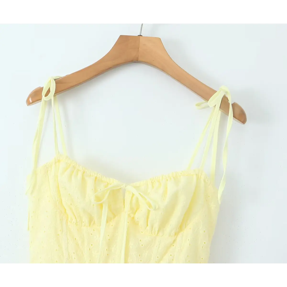 Close-up neck detail of pale yellow eyelet sundress, self-fabric tie spaghetti straps + shirred bust with front center bow.