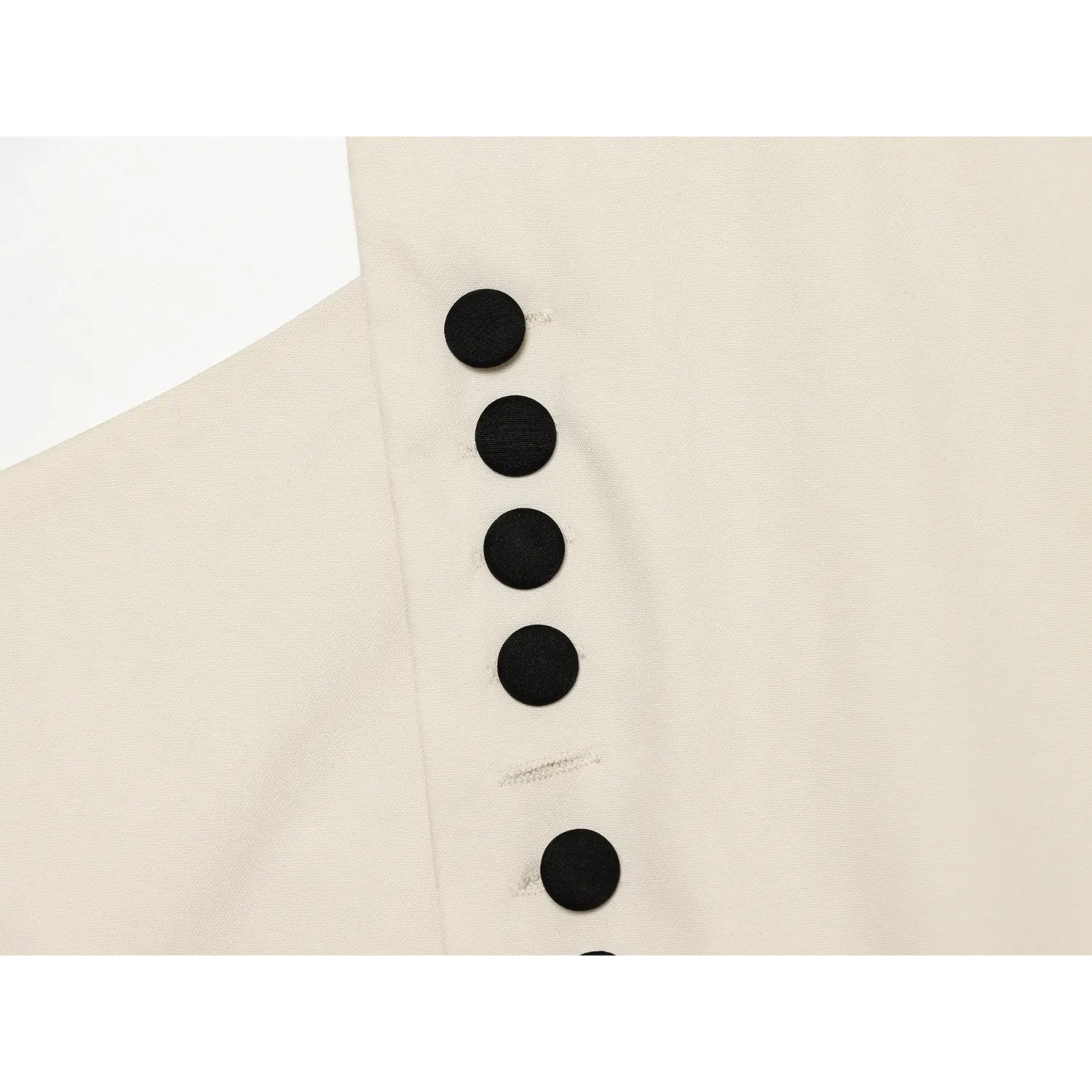 Macro shot of vertical black fabric buttons on cream wrap halter top