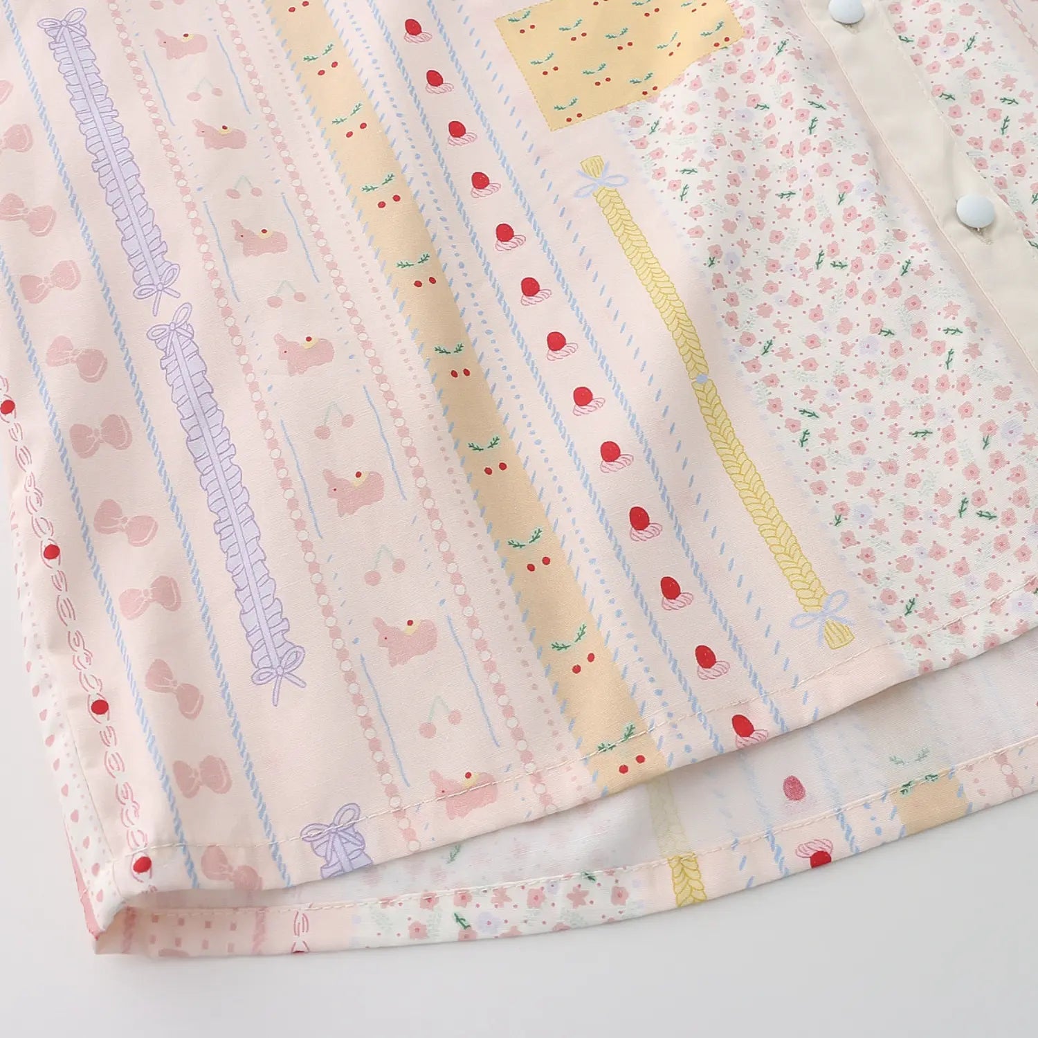 Blouse full vertical cartoon strip print fabric flat shot, macaron light pink base segmented prints of bunnies, ducks, cherries, florals and bows multi-color soft spliced print full pattern fabric display