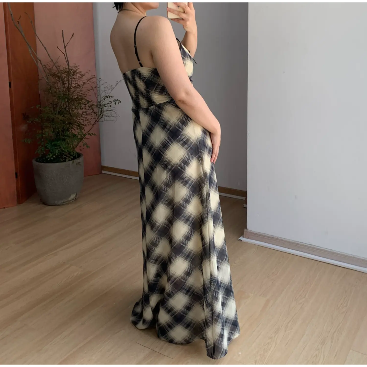 Back side indoor mirror shot of sheer chiffon plaid maxi dress, thin single adjustable spaghetti strap, full smocked elastic back waist for stretch fit, full flowy bias-cut skirt, cream & faded black diagonal check textile drape display