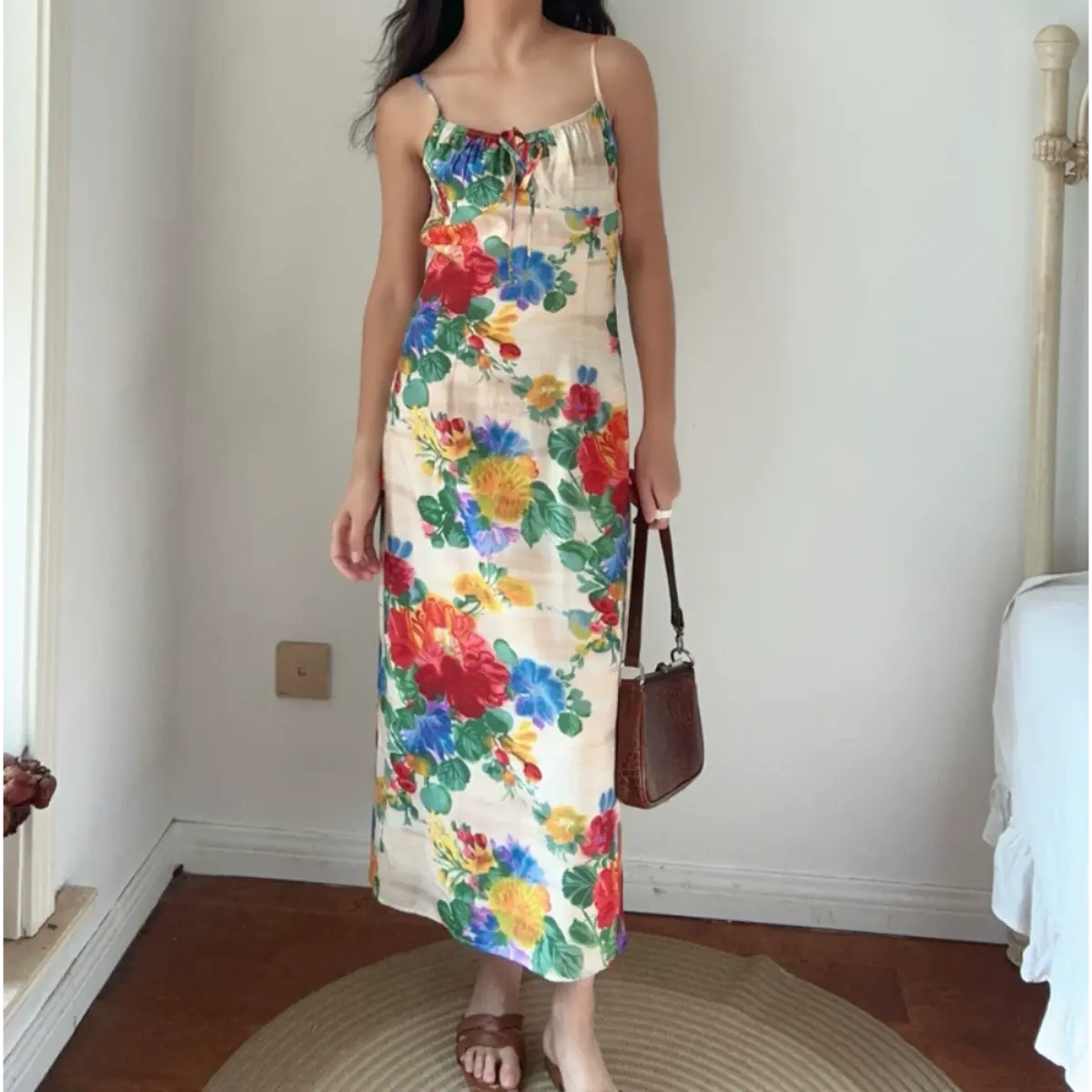 Front lifestyle shot of woman wearing vintage watercolor rose floral maxi slip dress with adjustable thin straps, paired with brown leather handbag and slide sandals.