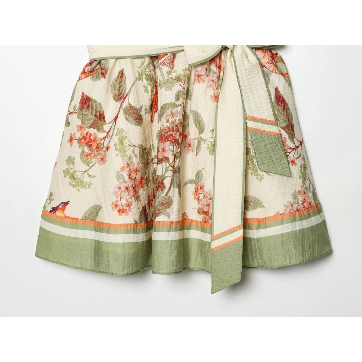 Hem close-up of off-white linen blend strapless mini dress, floral bird butterfly print with green stripe border hem and matching self-fabric sash tie.