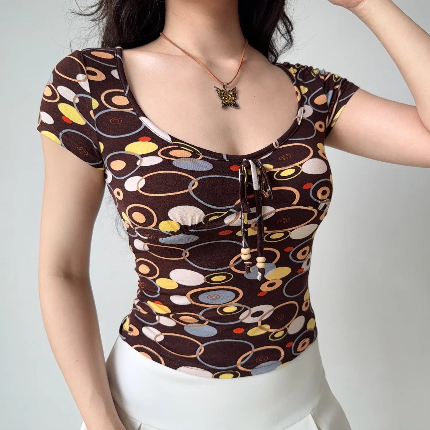 Close front shot of retro brown colorful circle print slim crop tee, front bead tie ruched bust low scoop neck cap sleeve top
