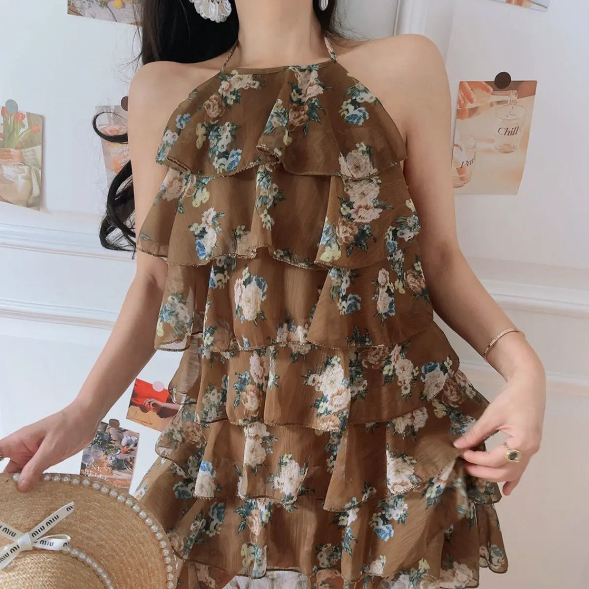Full front lifestyle shot of mocha base floral chiffon halter mini dress, multi-layer ruffle tiered skirt, matched with pearl straw hat for retro vacation outfit.