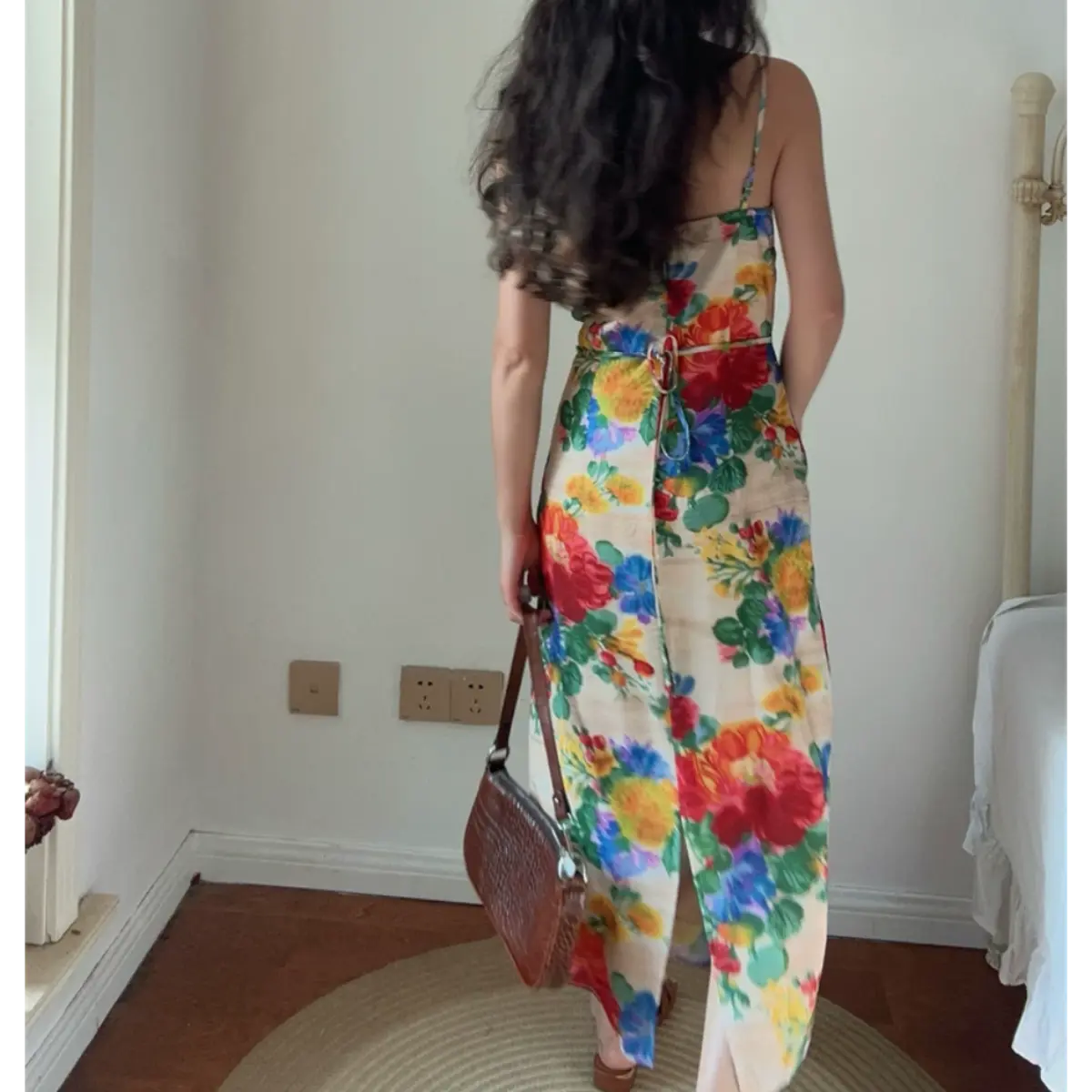 Back view lifestyle photo of vintage floral maxi dress, featuring waist self-tie closure and high back skirt split, colorful oversized flower print on cream base fabric.