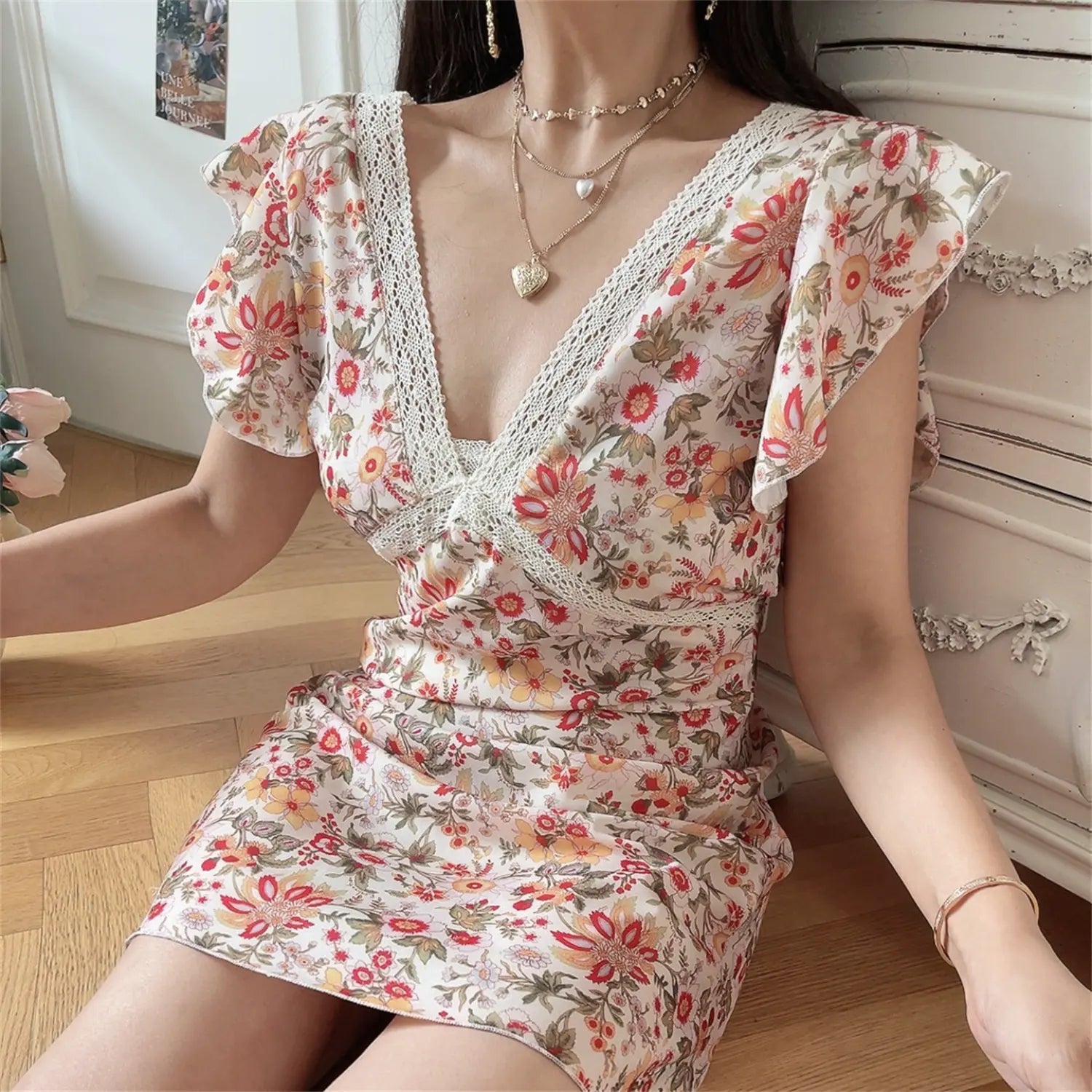 Lifestyle sitting shot women vintage floral mini dress, deep lace trim V neck, flutter ruffle cap sleeve, cream wildflower print slim wrap sundress