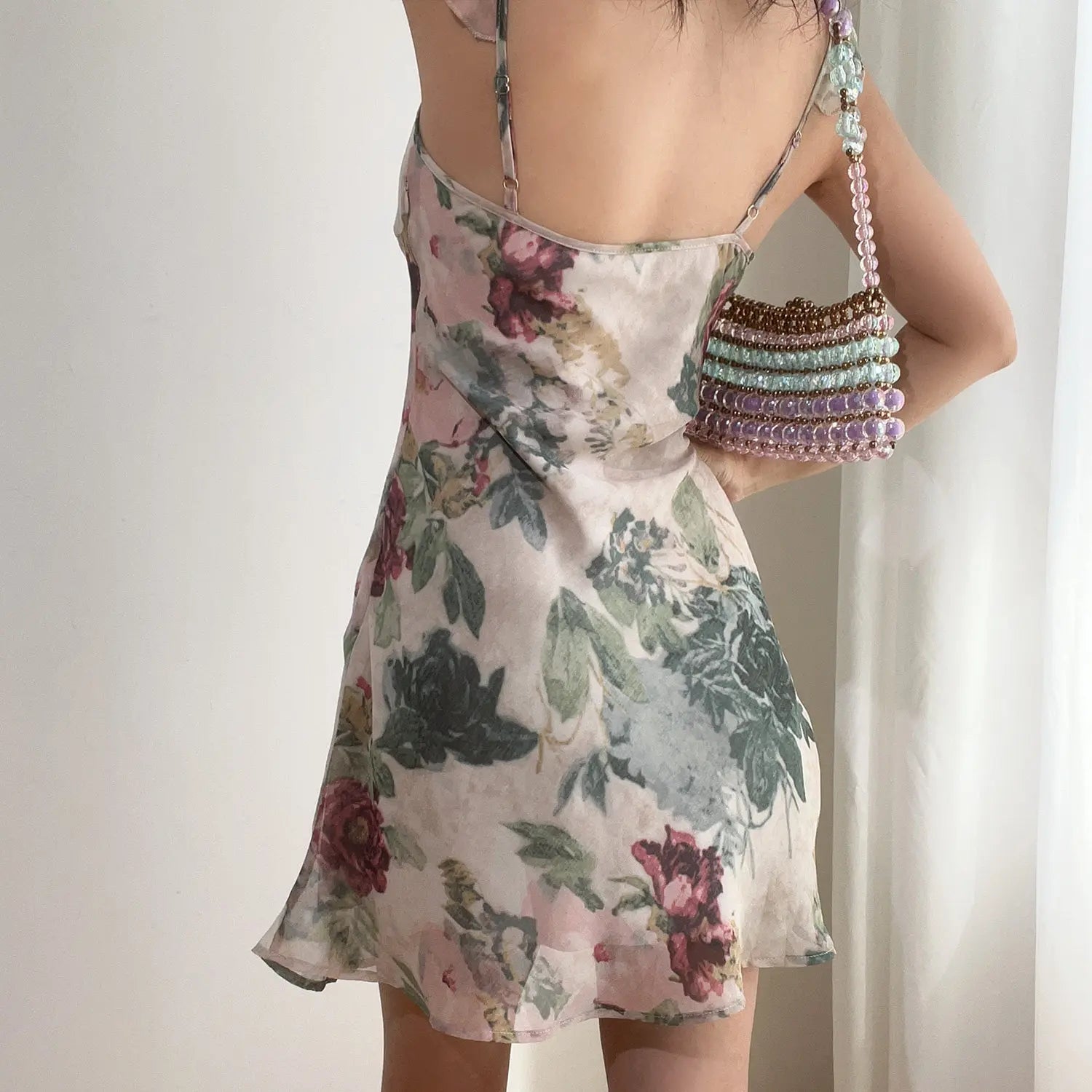 Model back view vintage floral mini dress, adjustable spaghetti straps and flowy skirt hem