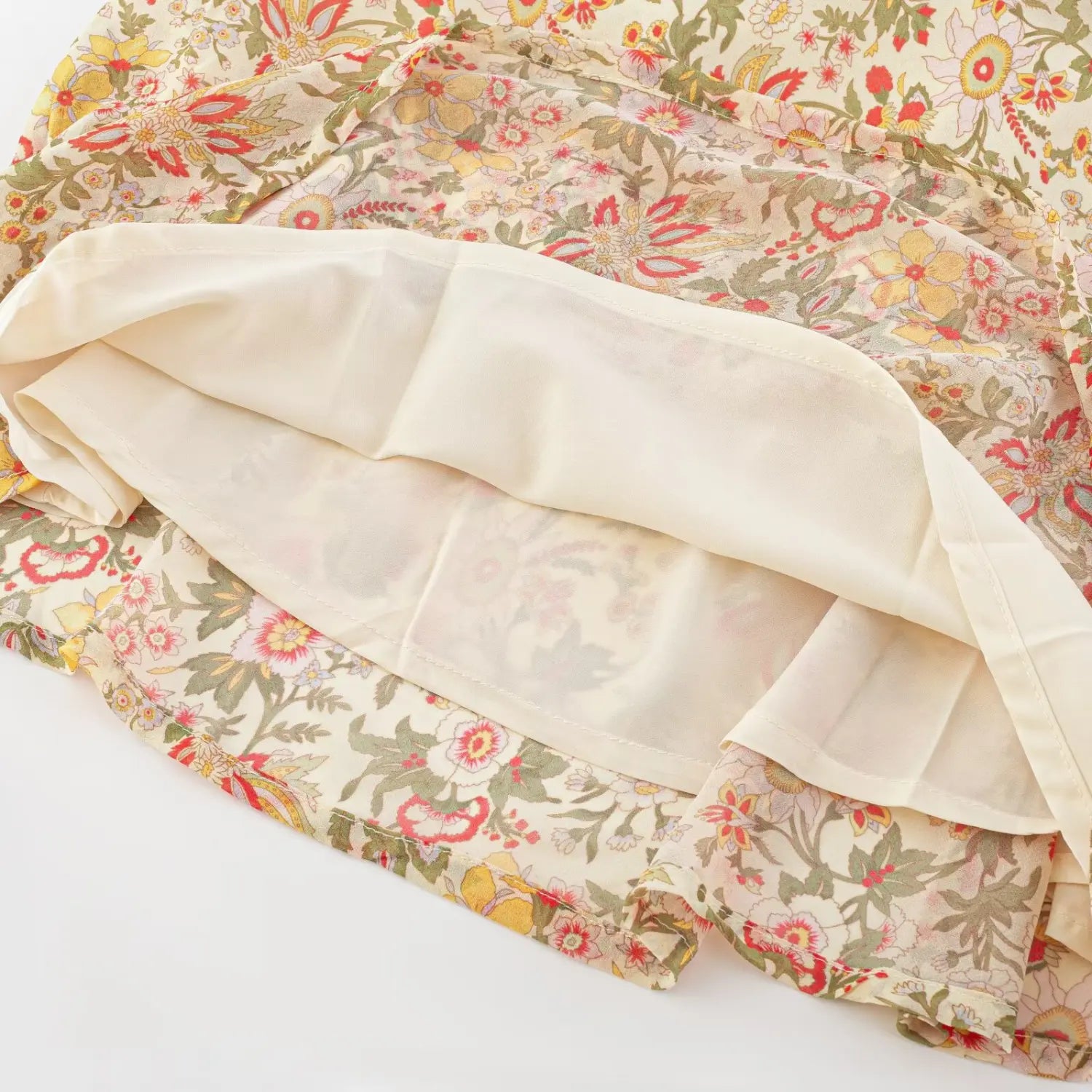 Top-down flat detail shot of floral chiffon mini skirt hem, folded open to show solid cream full lining and neat finished edge stitching