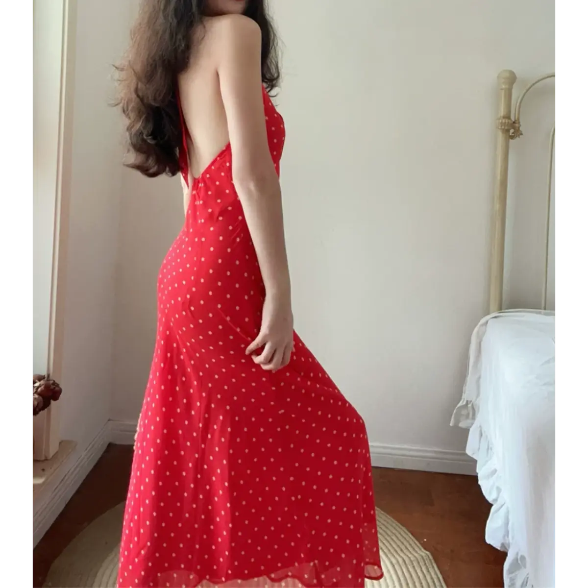 Back lifestyle photo of model in red cream polka dot halter midi dress, open back design, slim fit flowy chiffon skirt, retro vintage indoor outfit.