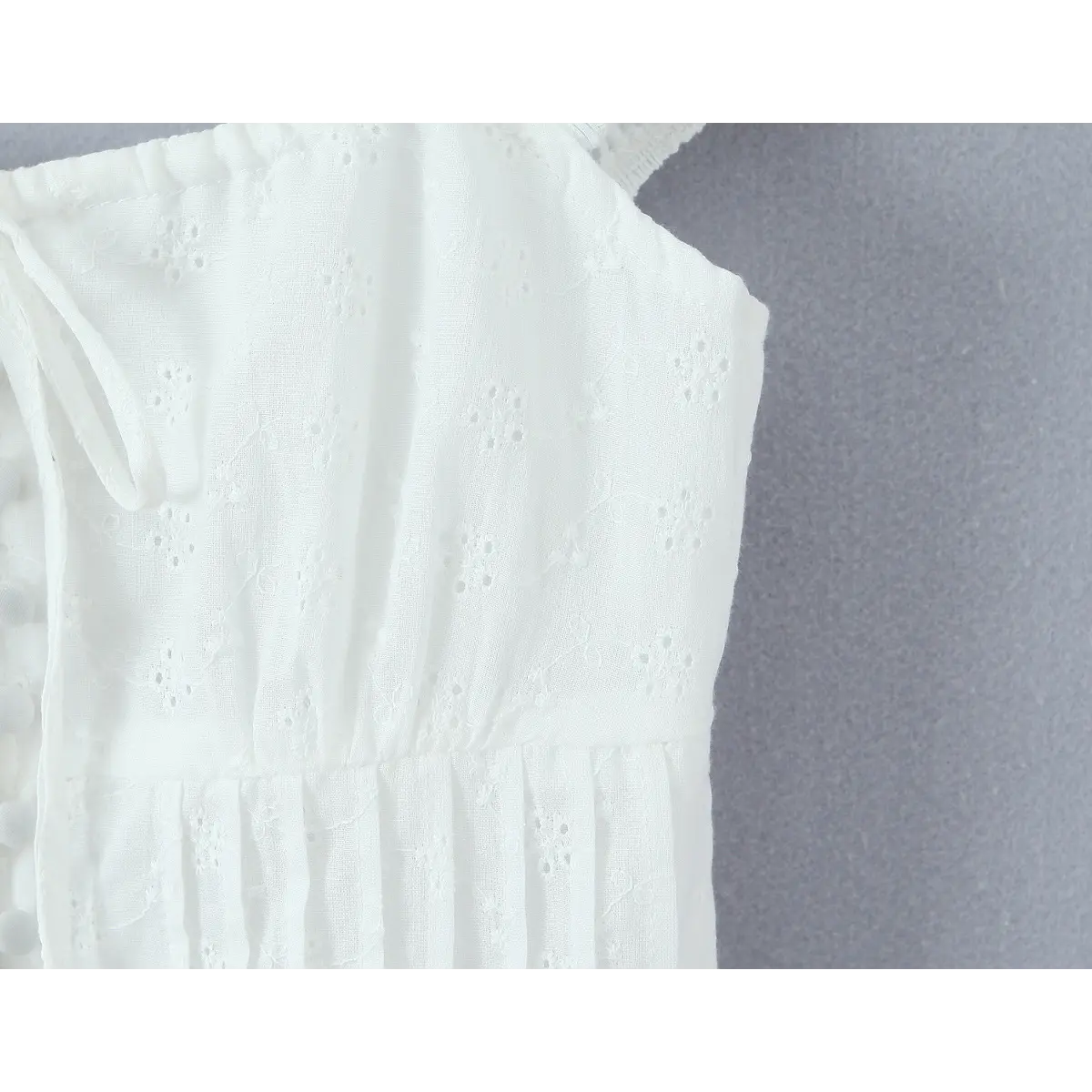 Close-up of the waist area of a white eyelet embroidered bustier top, showing the pintuck detailing and eyelet fabric texture.
