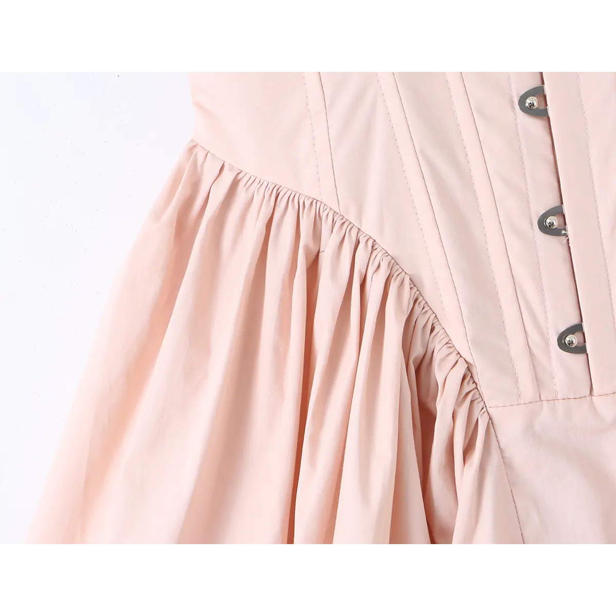 Close-up of the gathered waist seam and front metal eyelets on a light pink corset dress.
