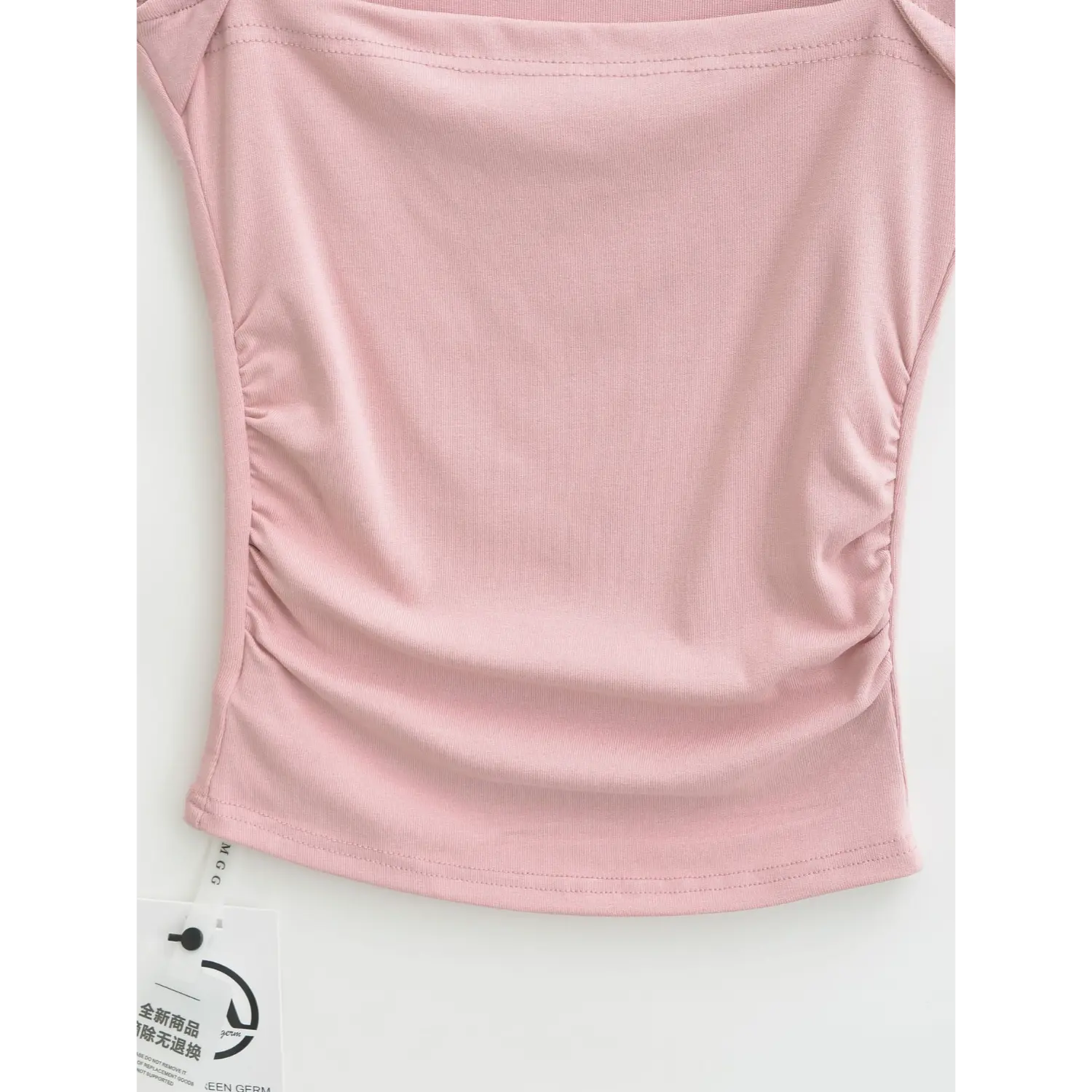 Front lower section shot showing side waist ruched gathering and curved bottom hem of dusty pink ribbed tank top with hang tag
