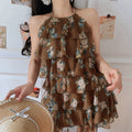 Front indoor lifestyle shot of mocha floral print tiered halter dress, irregular ruffle hem and flowy chiffon silhouette.