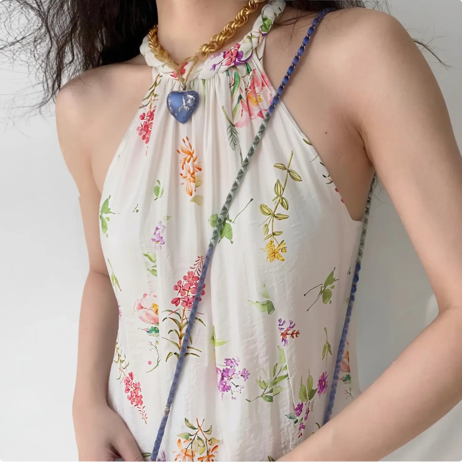 Lifestyle model shot wearing floral braided halter tank top, paired with thick gold heart pendant chain and woven blue crossbody bag, soft casual summer styling
