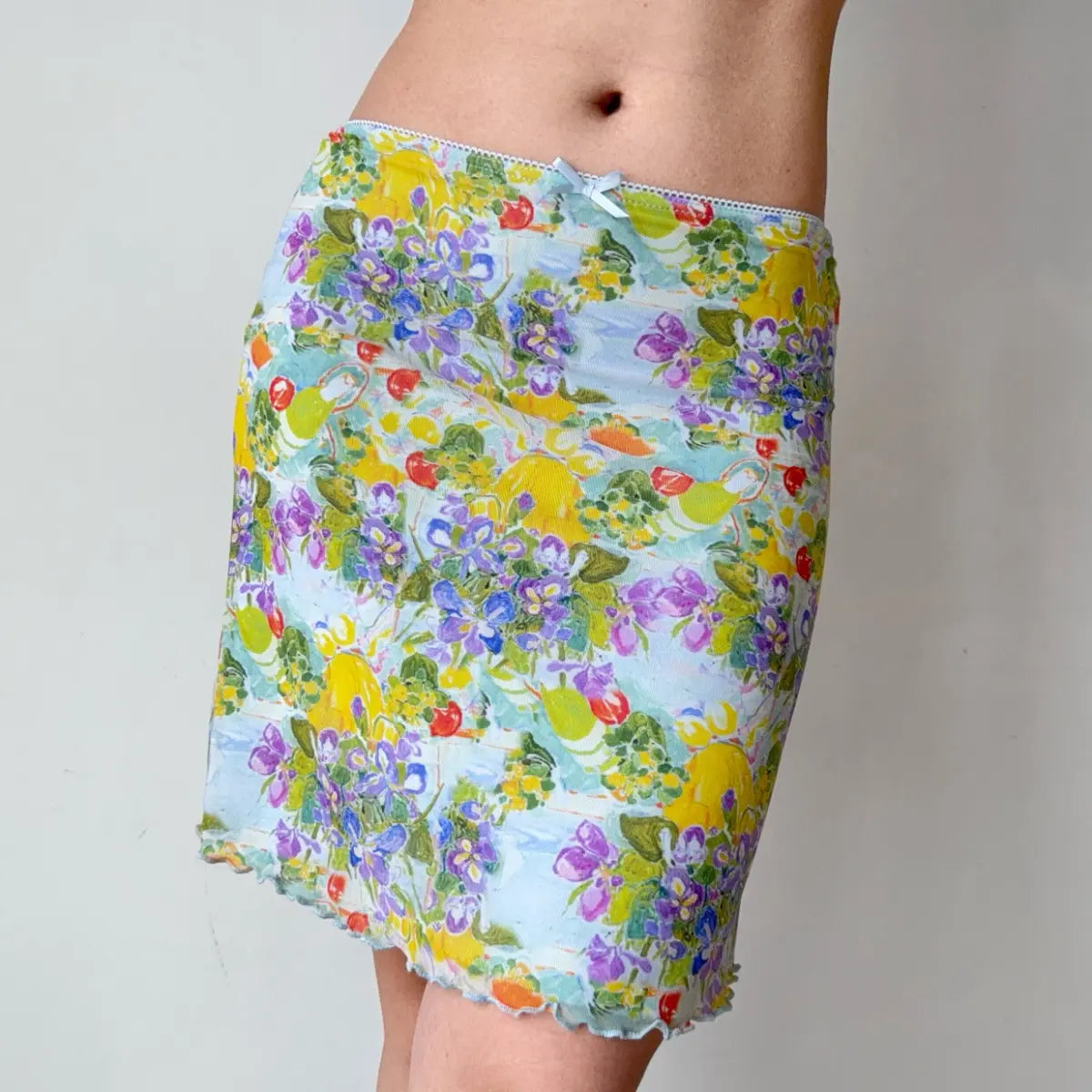 Angled view of a light blue mesh mini skirt showcasing the watercolor print, form-fitting silhouette, and lettuce-edge hem.