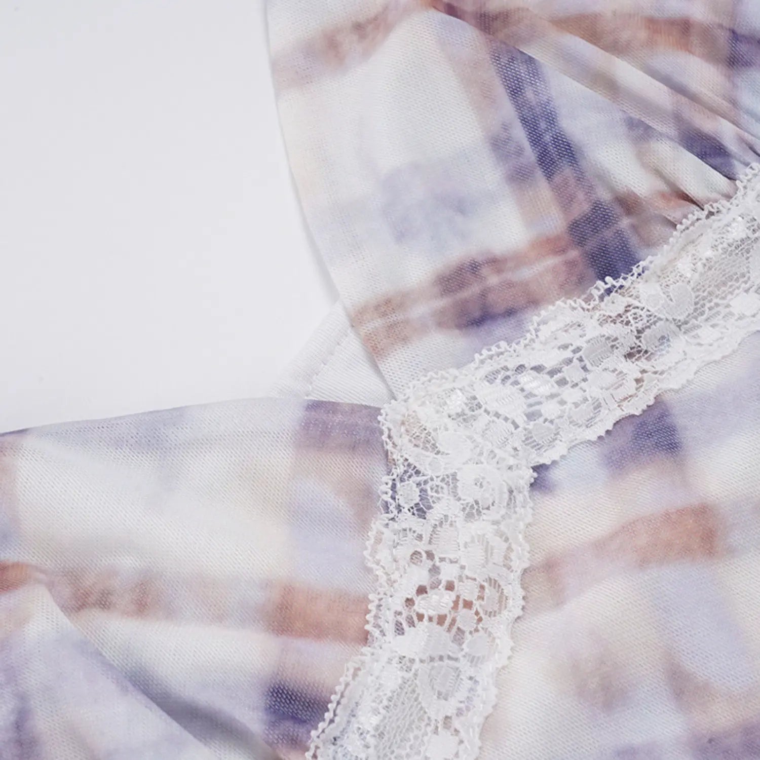 Partial flat close-up of slip dress underbust construction, ornate white floral lace trim sewn between V-neck bust and mesh skirt, sheer printed mesh outer layer over solid lining