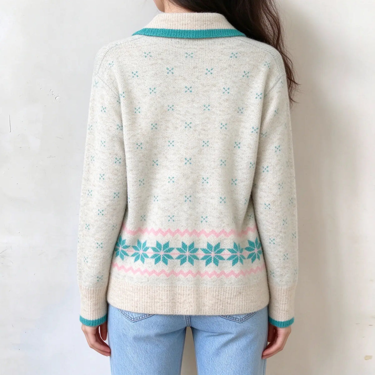 Back view of female model in cream knit zip cardigan, small teal dot patterns all over back, pink wavy lines and turquoise snowflake border at hem, teal collar and cuff trim