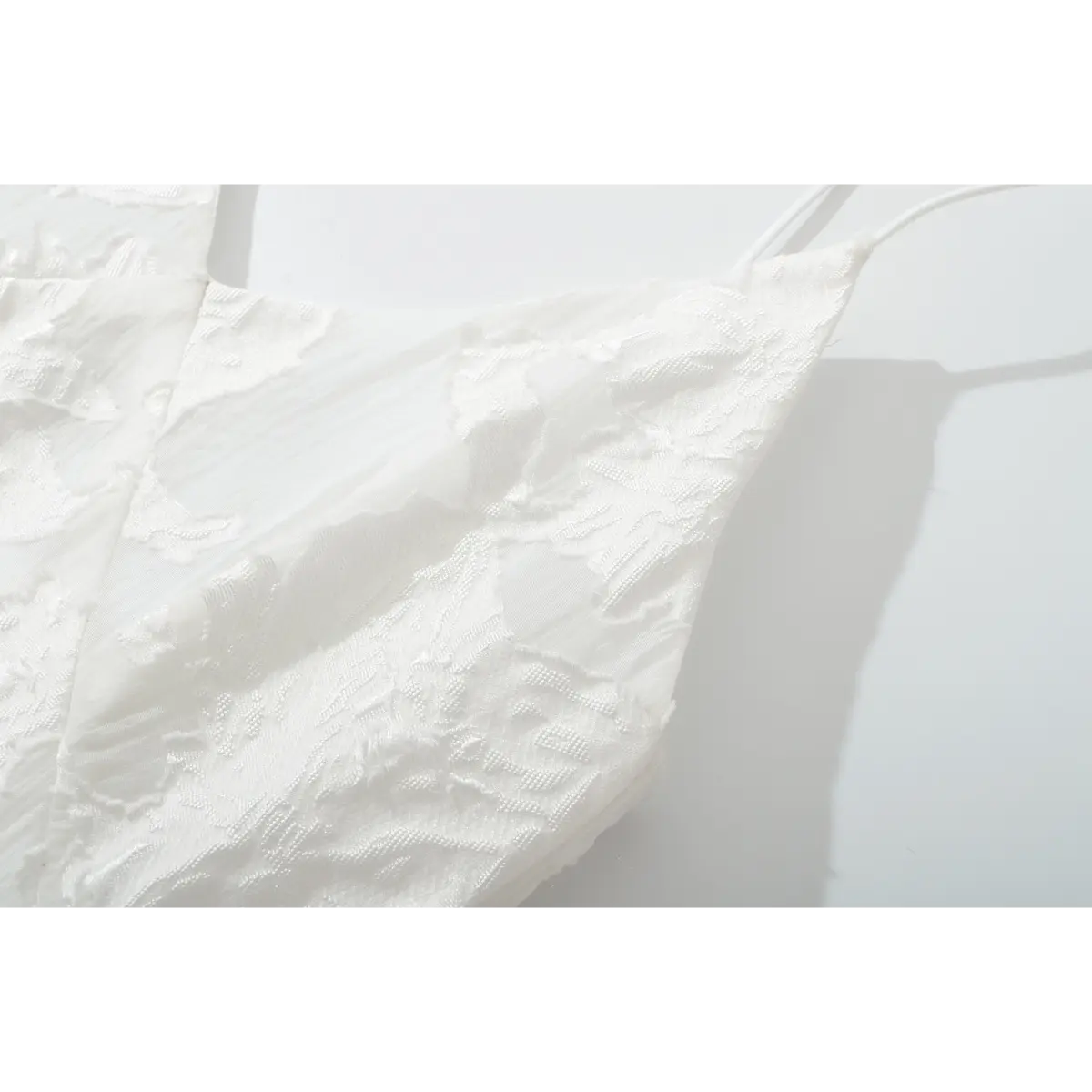 Closeup of raised floral jacquard fabric on white cami dress bust