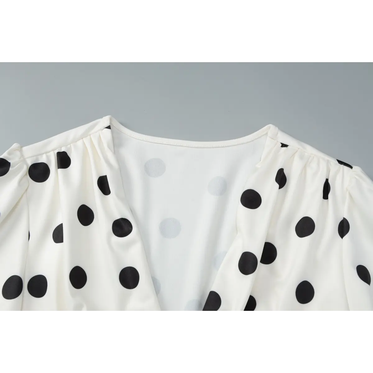 Close-up view of the V-neckline, gathered shoulders, and puffed short sleeves on the polka dot dress.