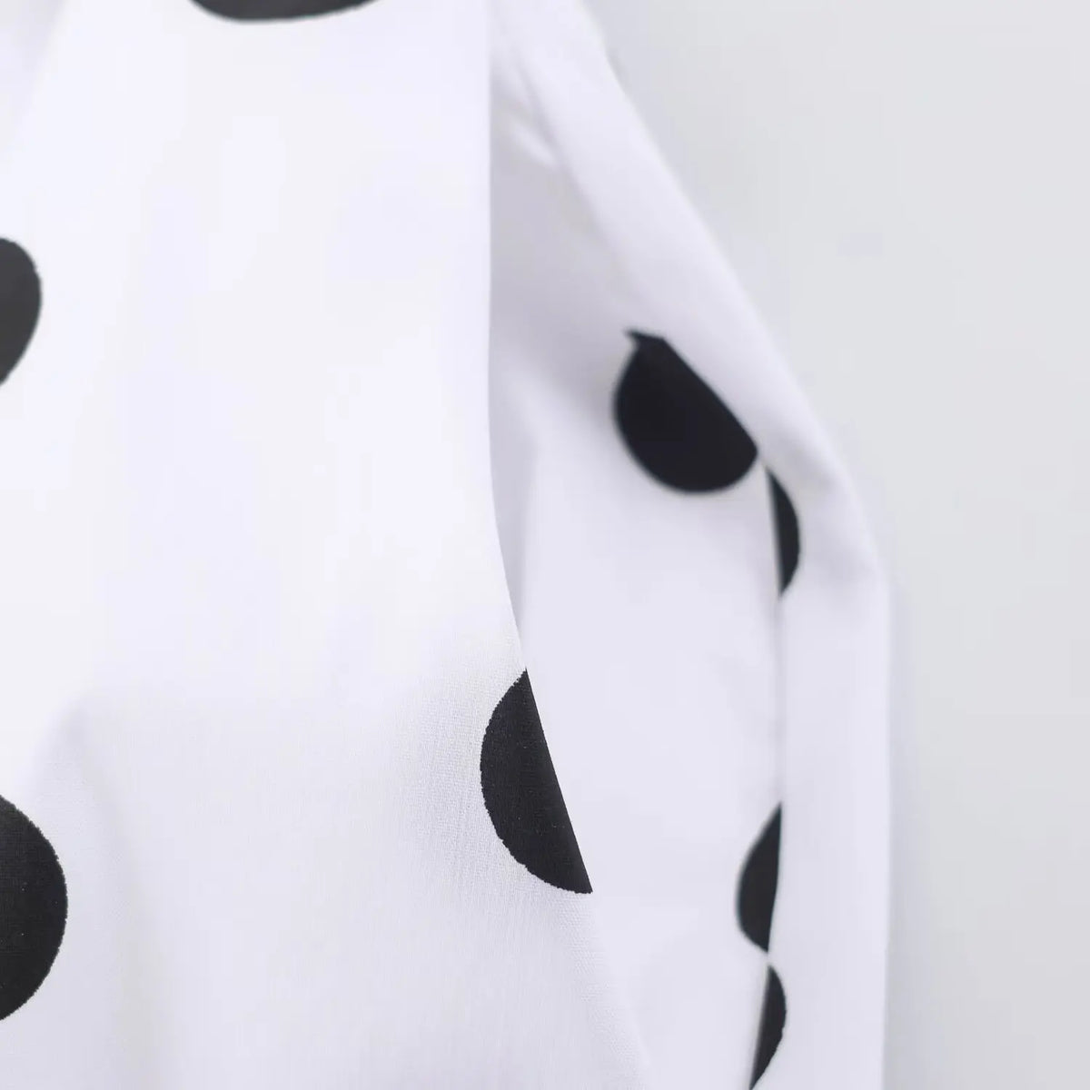 Close‑up fabric texture of white dress with black polka dot print