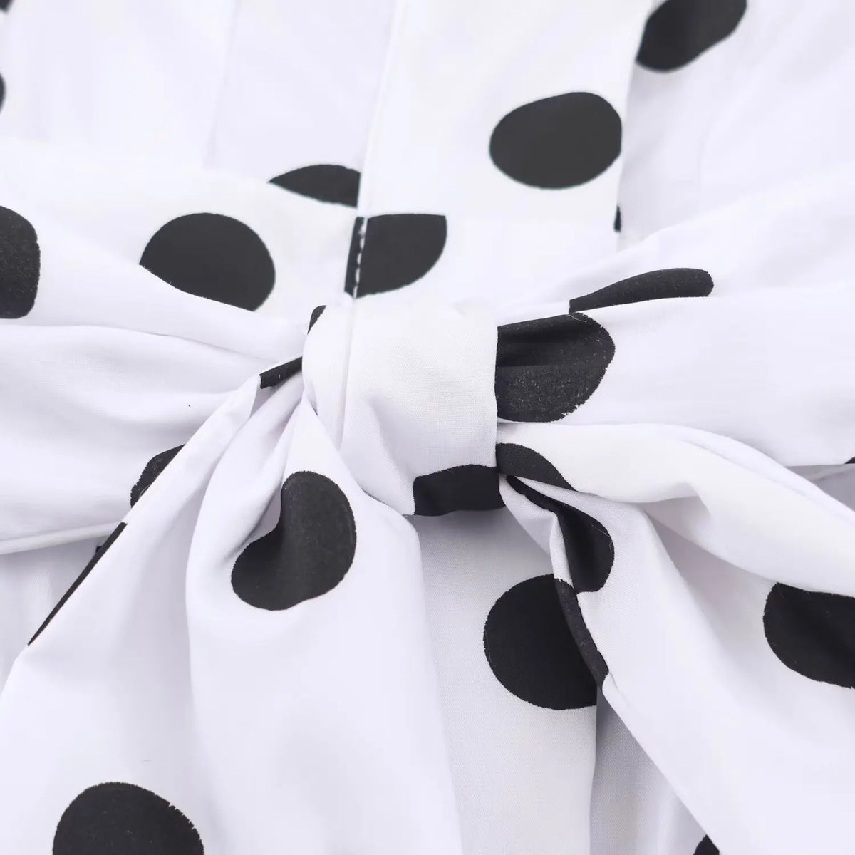 Close‑up self fabric tie bow at waist of white black polka dot maxi dress