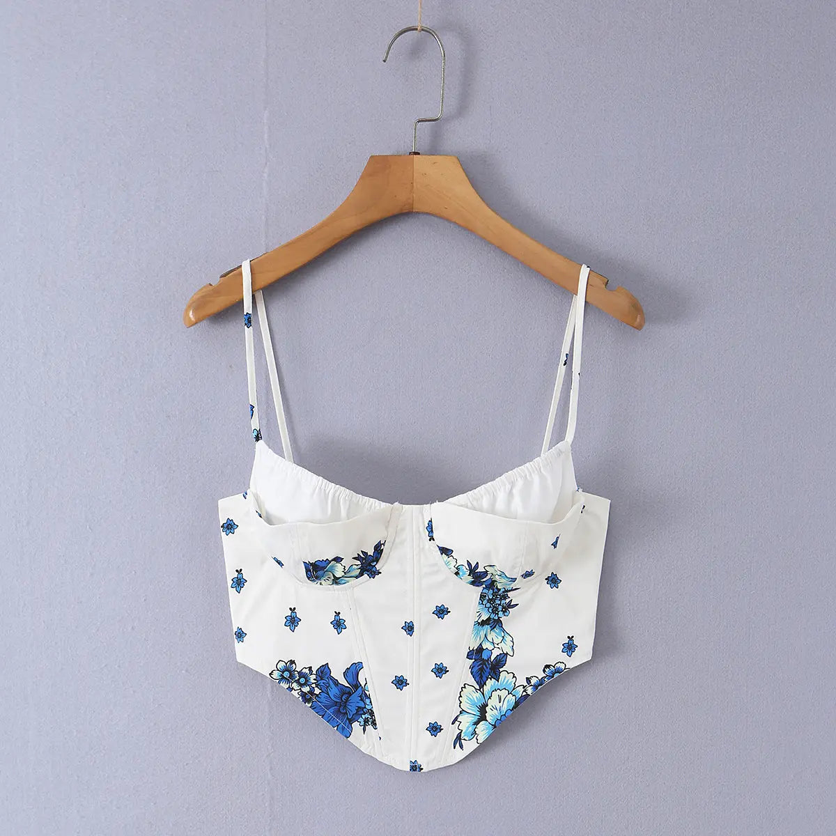 White cami top with blue floral print and tie closure, hanging on wooden hanger