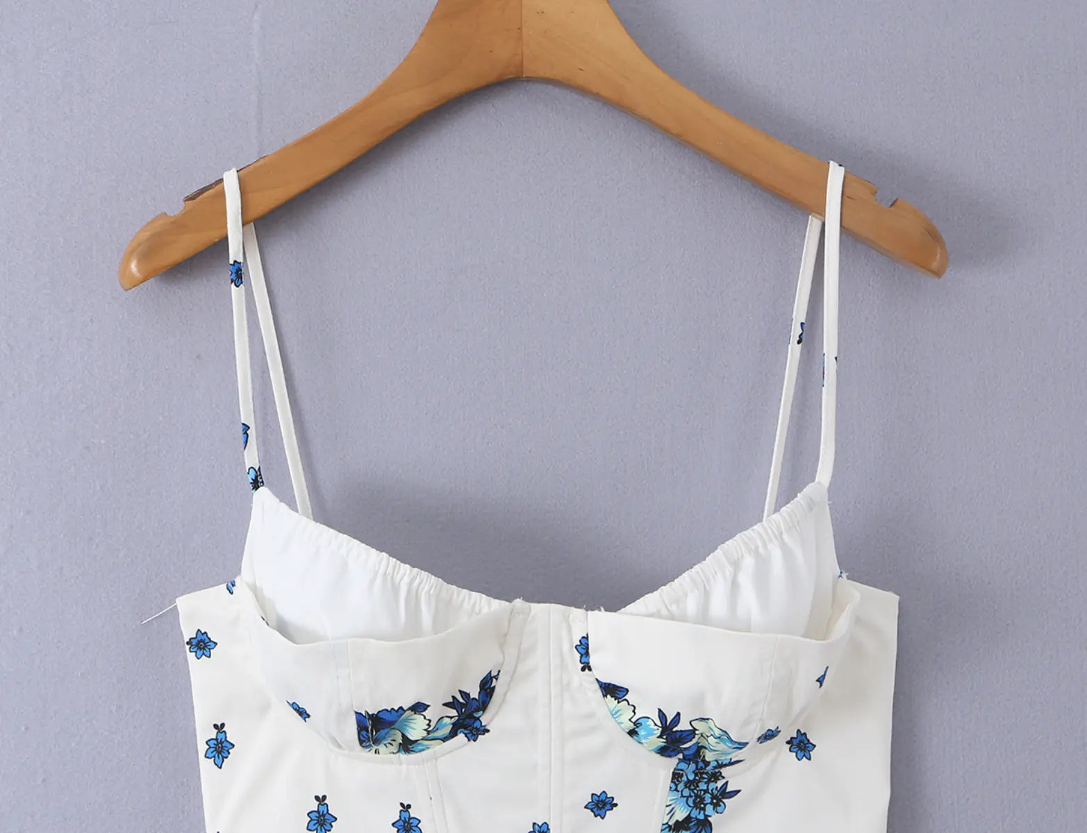 White corset-style cami top with blue floral print, full front view on wooden hanger